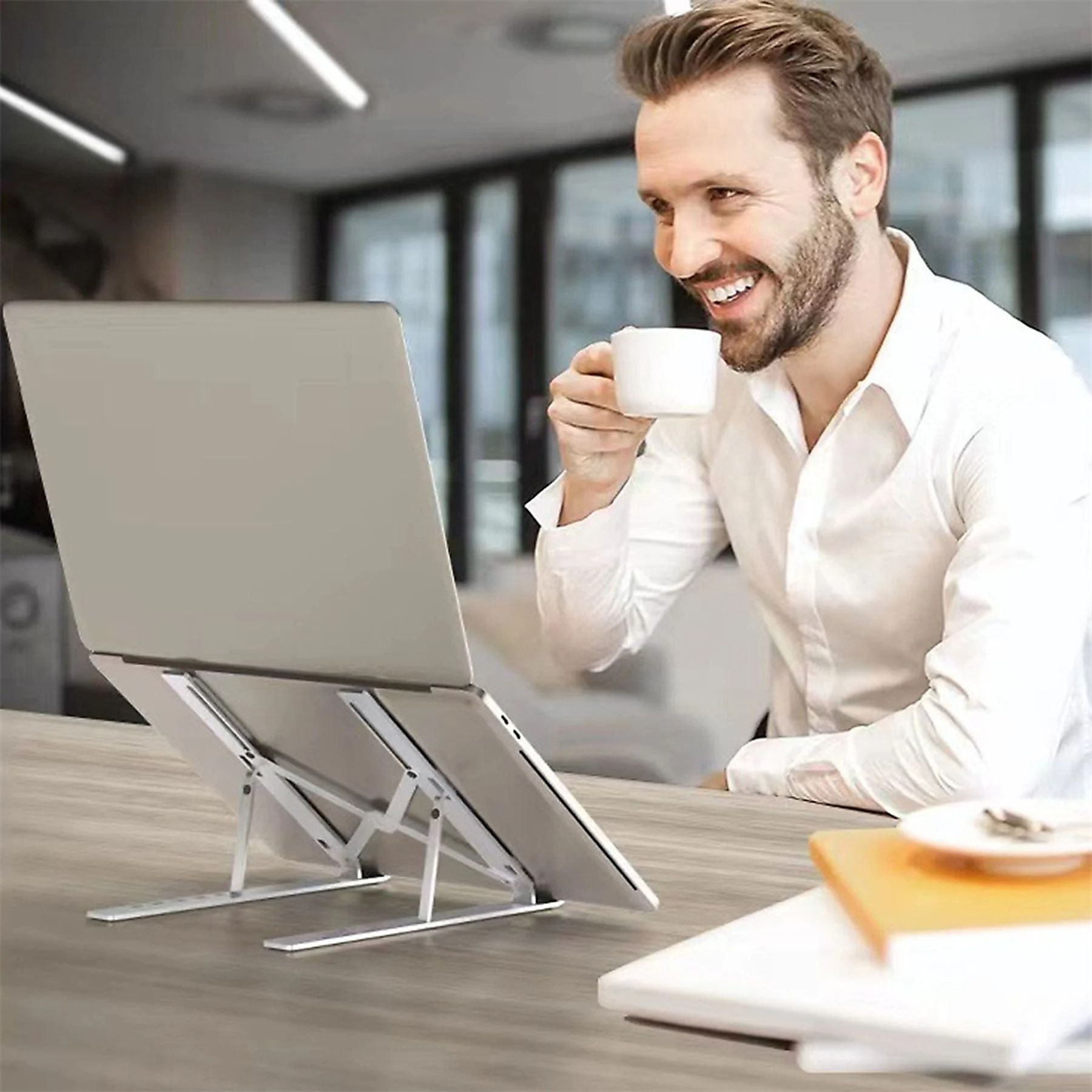 Mann, der Laptop auf Ständer benutzt, Kaffee trinkt.