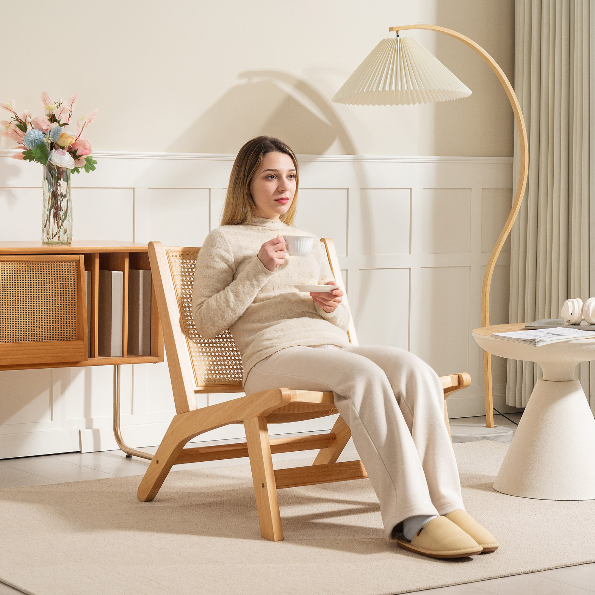Mujer sentada en una silla de madera, sosteniendo una taza, en una habitación luminosa.