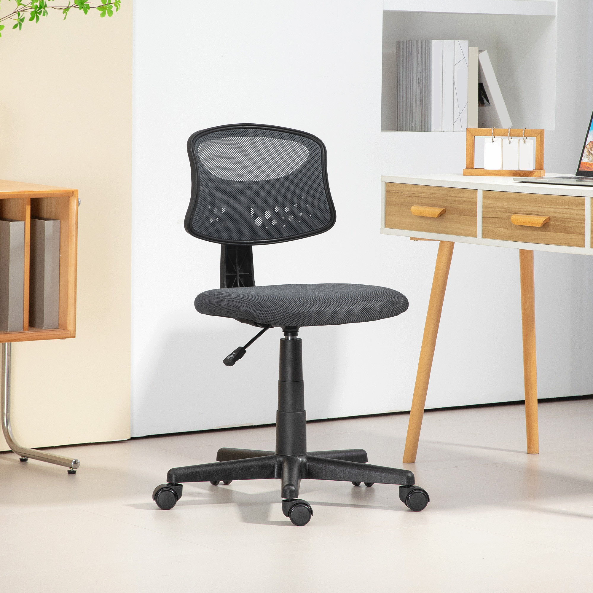 Silla de oficina con respaldo de malla. La silla es negra, el fondo tiene escritorio y estantes.