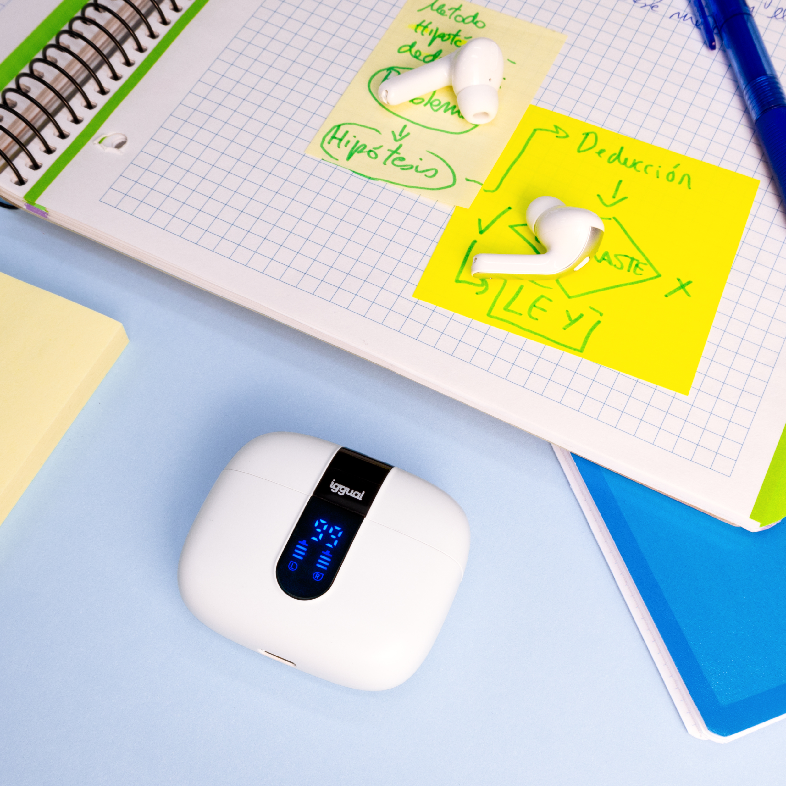 Custodia per auricolari bianca con display, blocco note, post-it e auricolari su superficie blu.