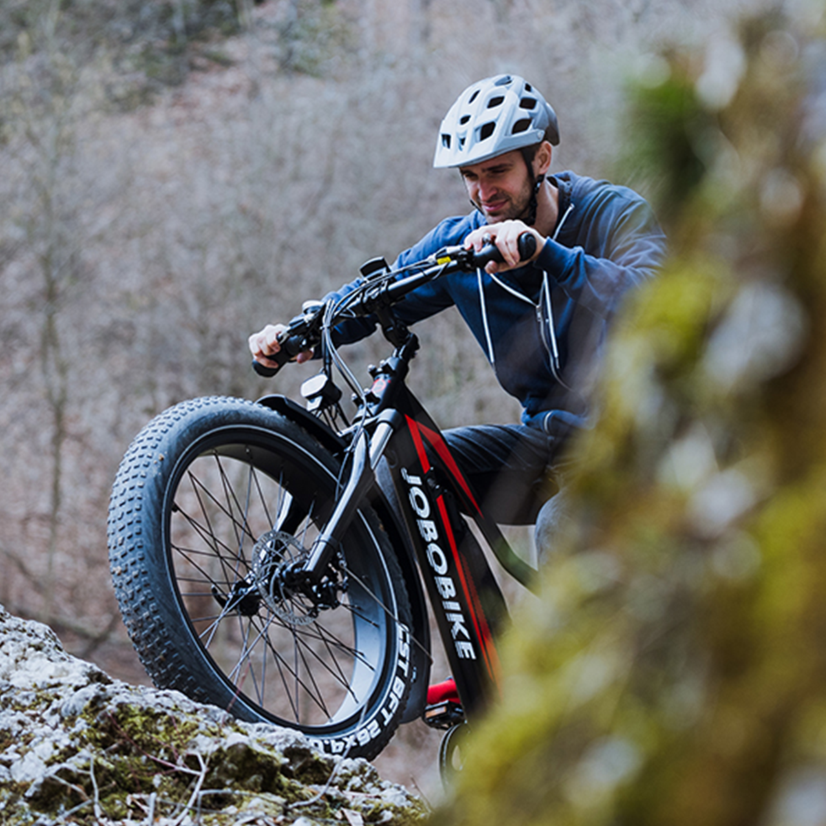 Ein Mann fährt mit einem Fatbike auf einem steinigen Weg, blickt nach vorne, trägt einen Helm.