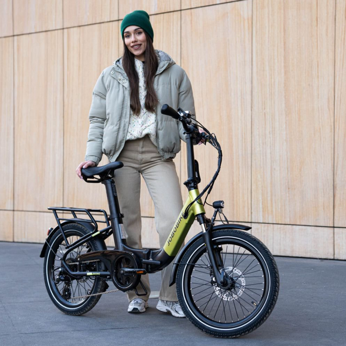 Kobieta stojąca z rowerem elektrycznym. Ma na sobie kapelusz i kurtkę.
