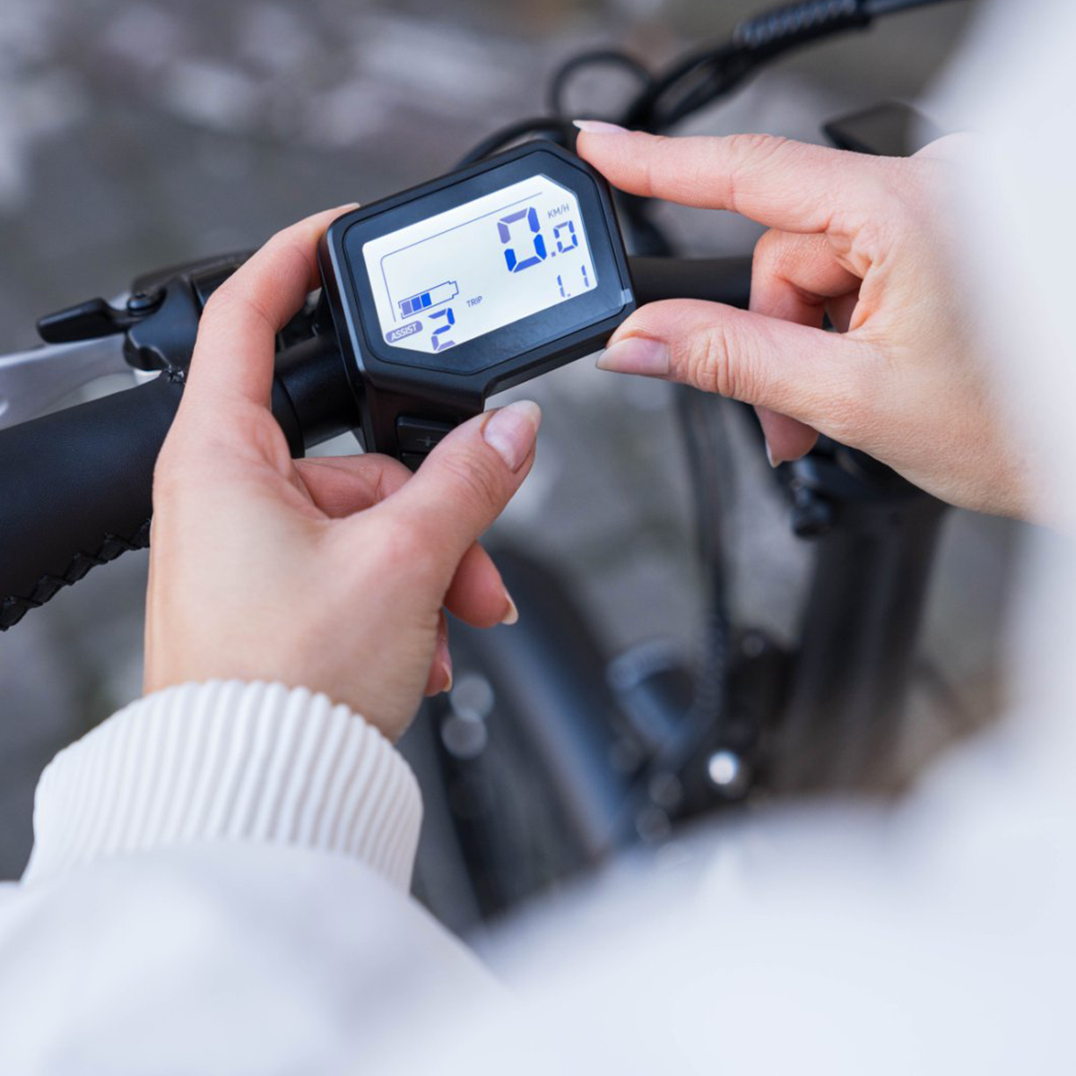 Ręce regulujące wyświetlacz e-bike, pokazujący prędkość i inne informacje.