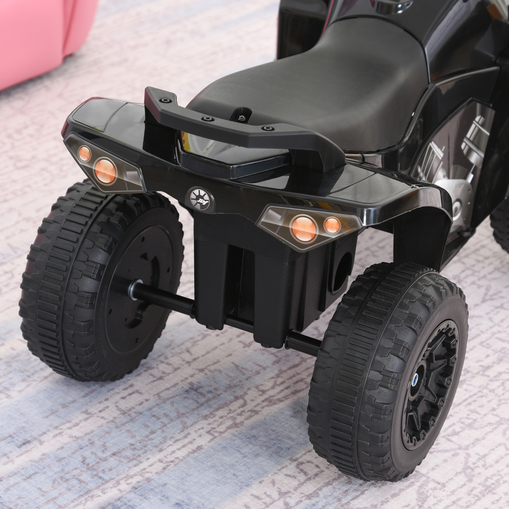 Primer plano de la parte trasera de un juguete ATV negro, que muestra las ruedas y las luces. Superficie gris claro.