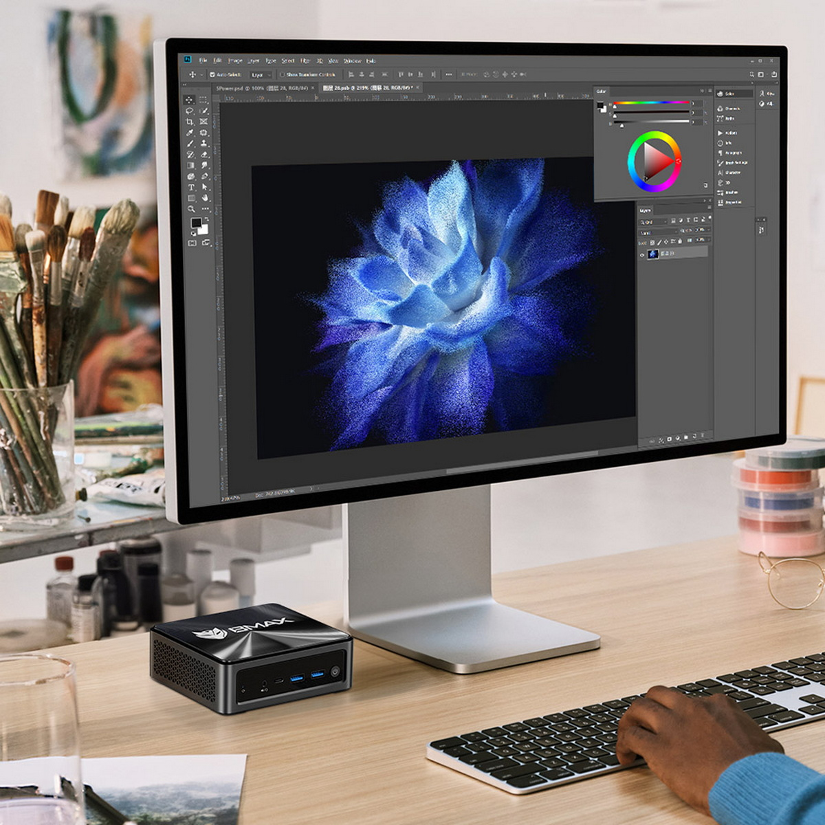 Ekran komputera z wyświetlonym obrazem sztuki cyfrowej. Mały czarny komputer stoi na biurku.
