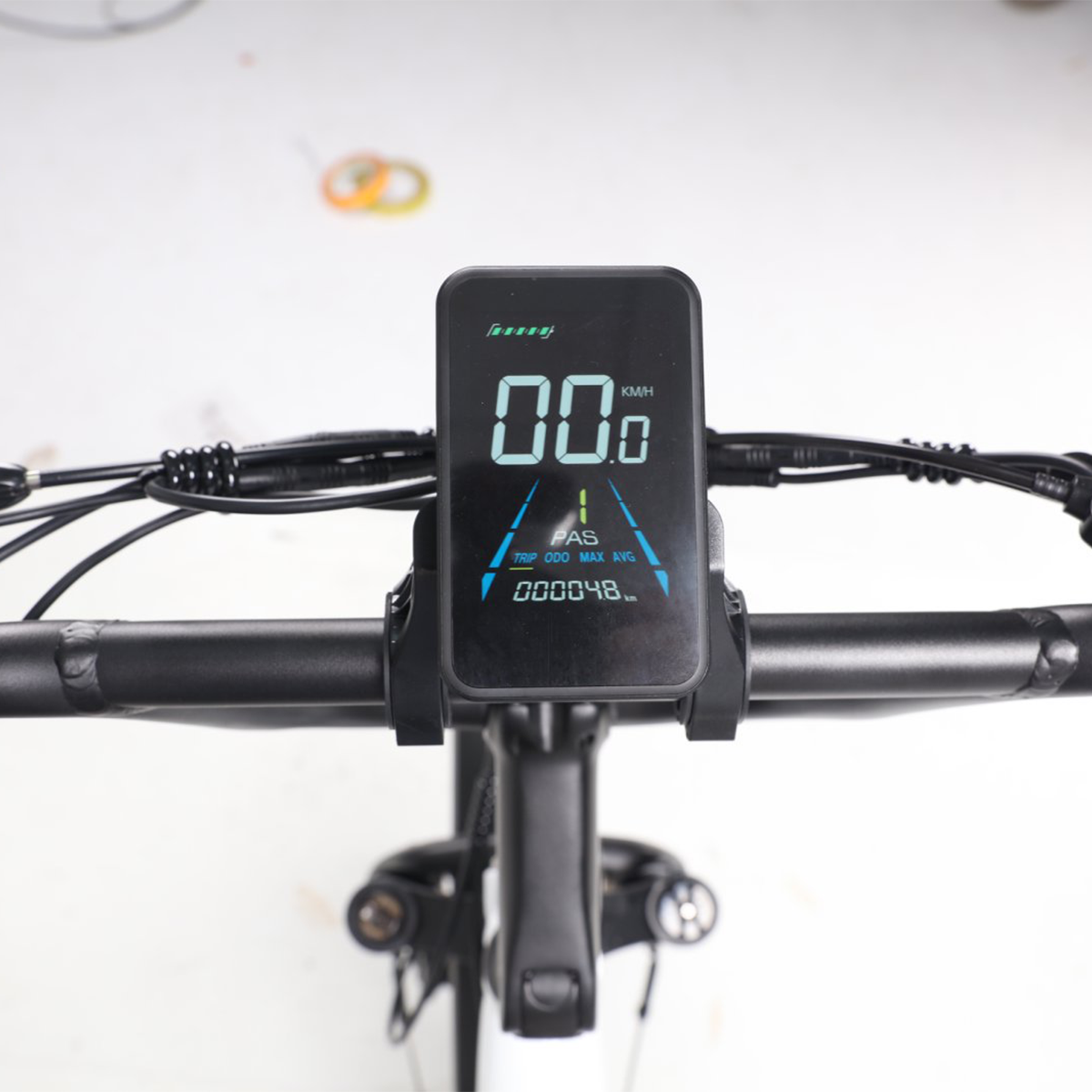 Zbliżenie wyświetlacza roweru pokazującego prędkość, dystans i inne wskaźniki. Widoczna kierownica i elementy sterowania.