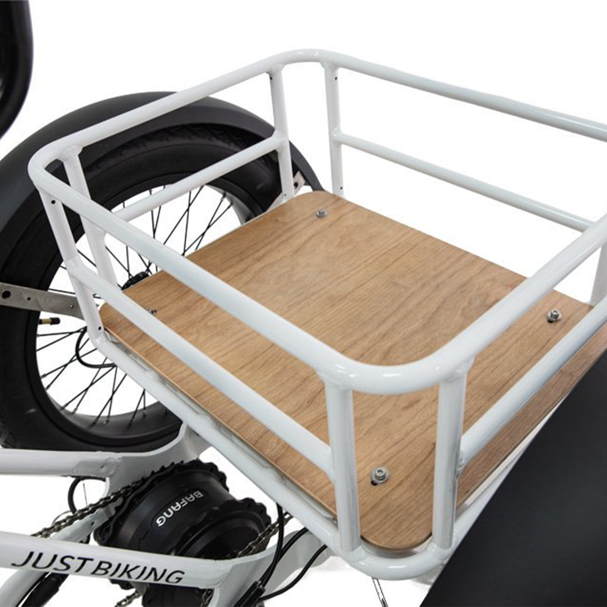 Biały bagażnik rowerowy z drewnianą podstawą. Widoczne czarne koło i opona. Marka to JUST BIKING.