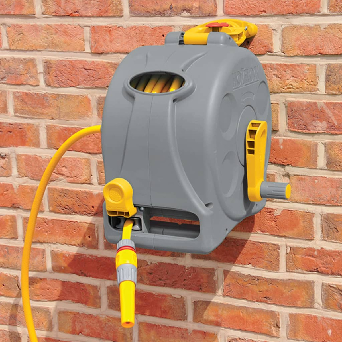 Carrete de manguera gris y amarillo montado en una pared de ladrillo. Se adjunta una manguera y boquilla amarilla.