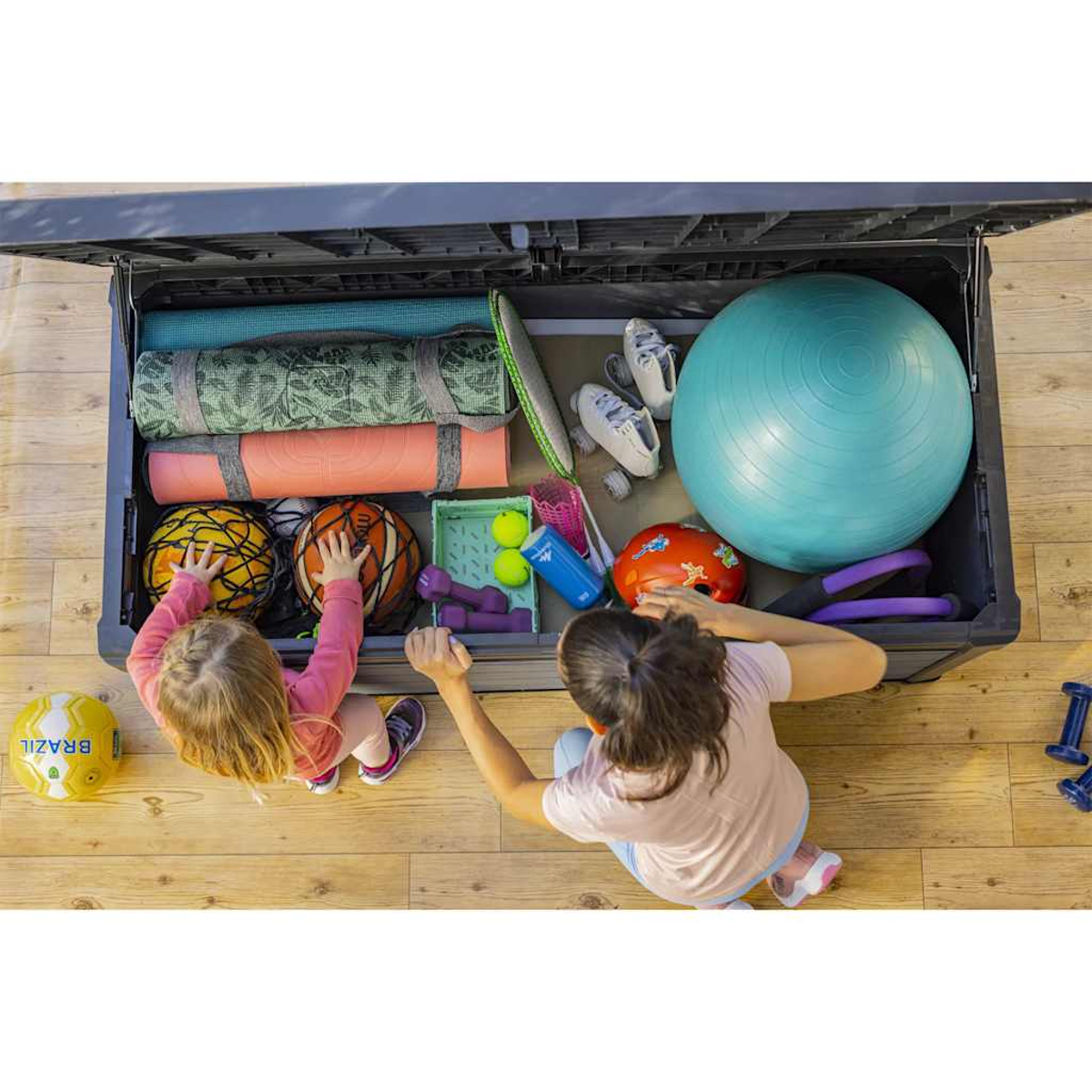 Zwei Kinder öffnen eine Aufbewahrungsbox mit Sportgeräten und Bällen.