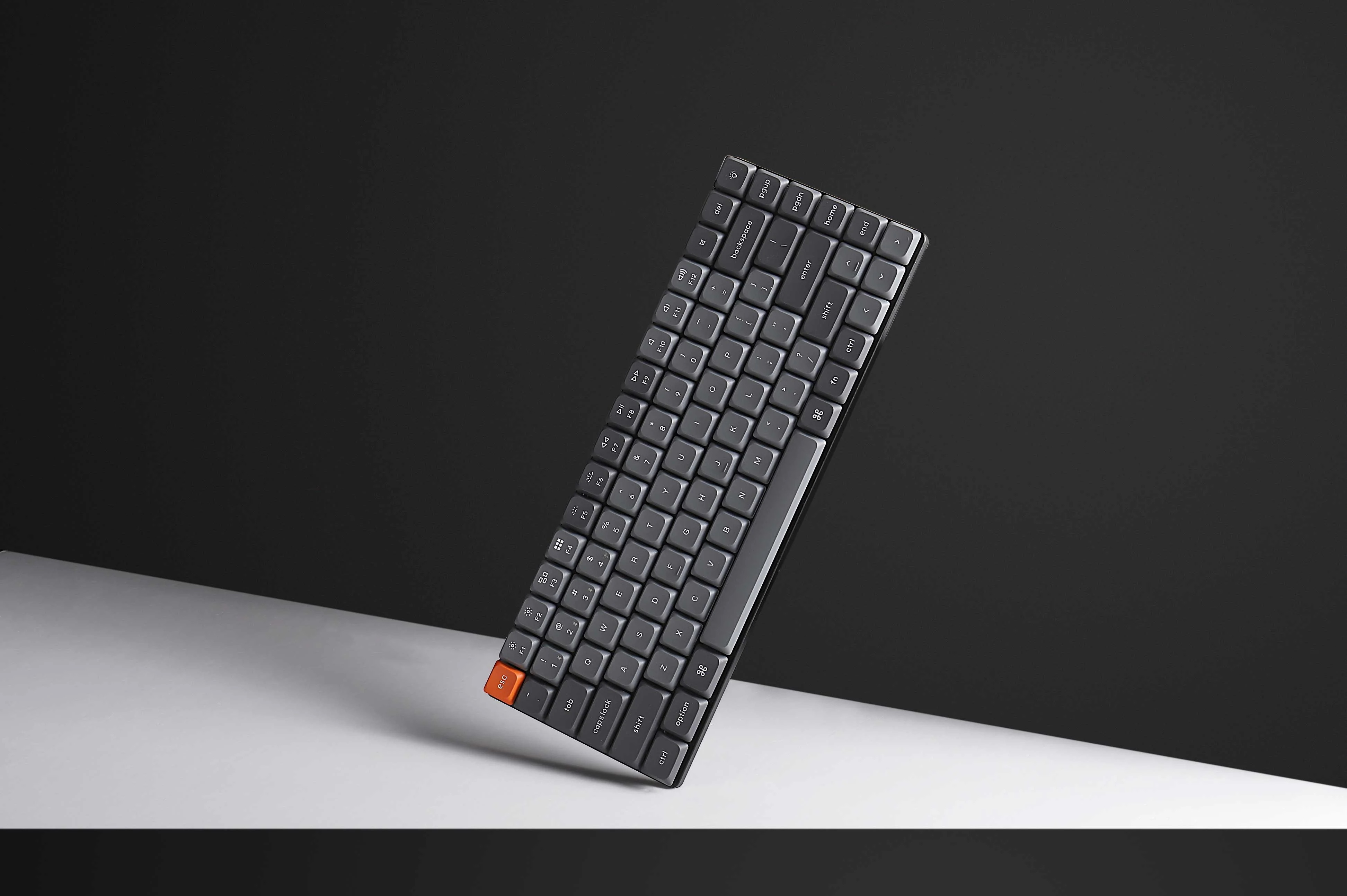 Widok pod kątem klawiatury mechanicznej z ciemnymi klawiszami i pomarańczowym klawiszem Escape.