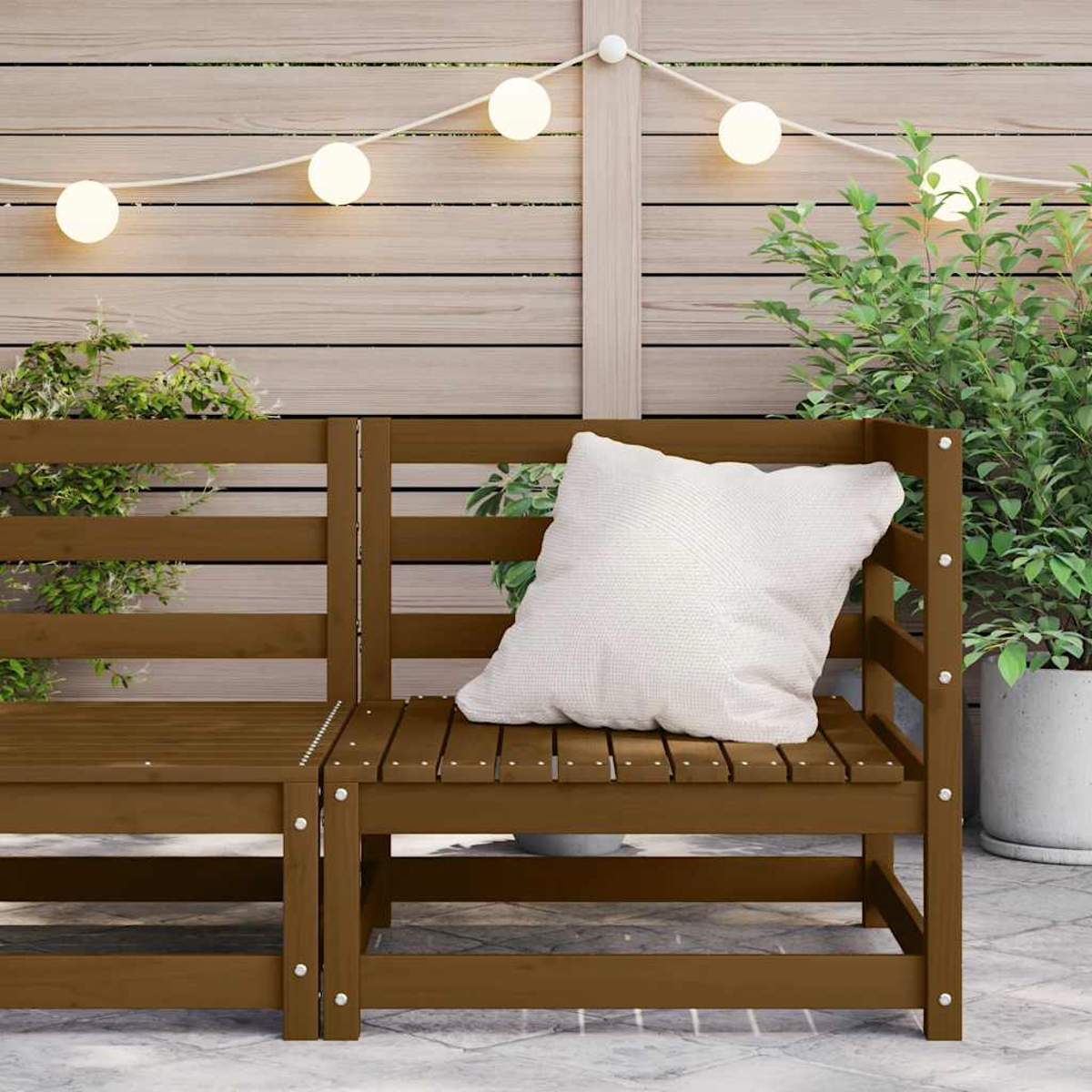 Gartenbank mit weißem Kissen, Holzzaun im Hintergrund und Lichterketten.