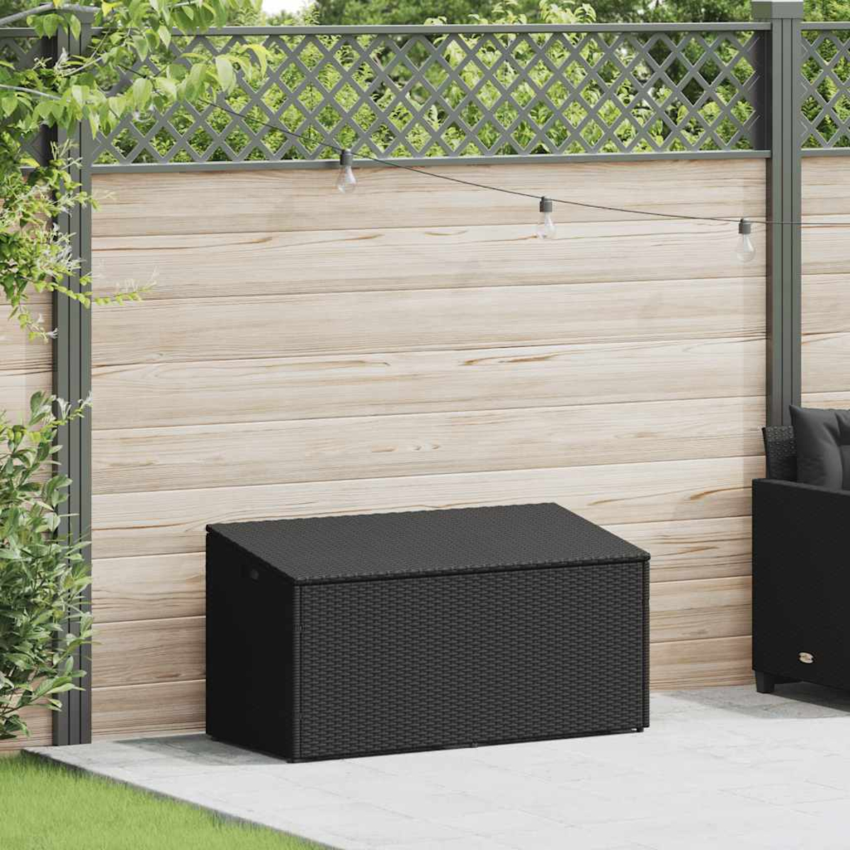 Eine schwarze Rattan-Aufbewahrungsbox vor einem Holzzaun. Ein grauer Patio ist sichtbar.
