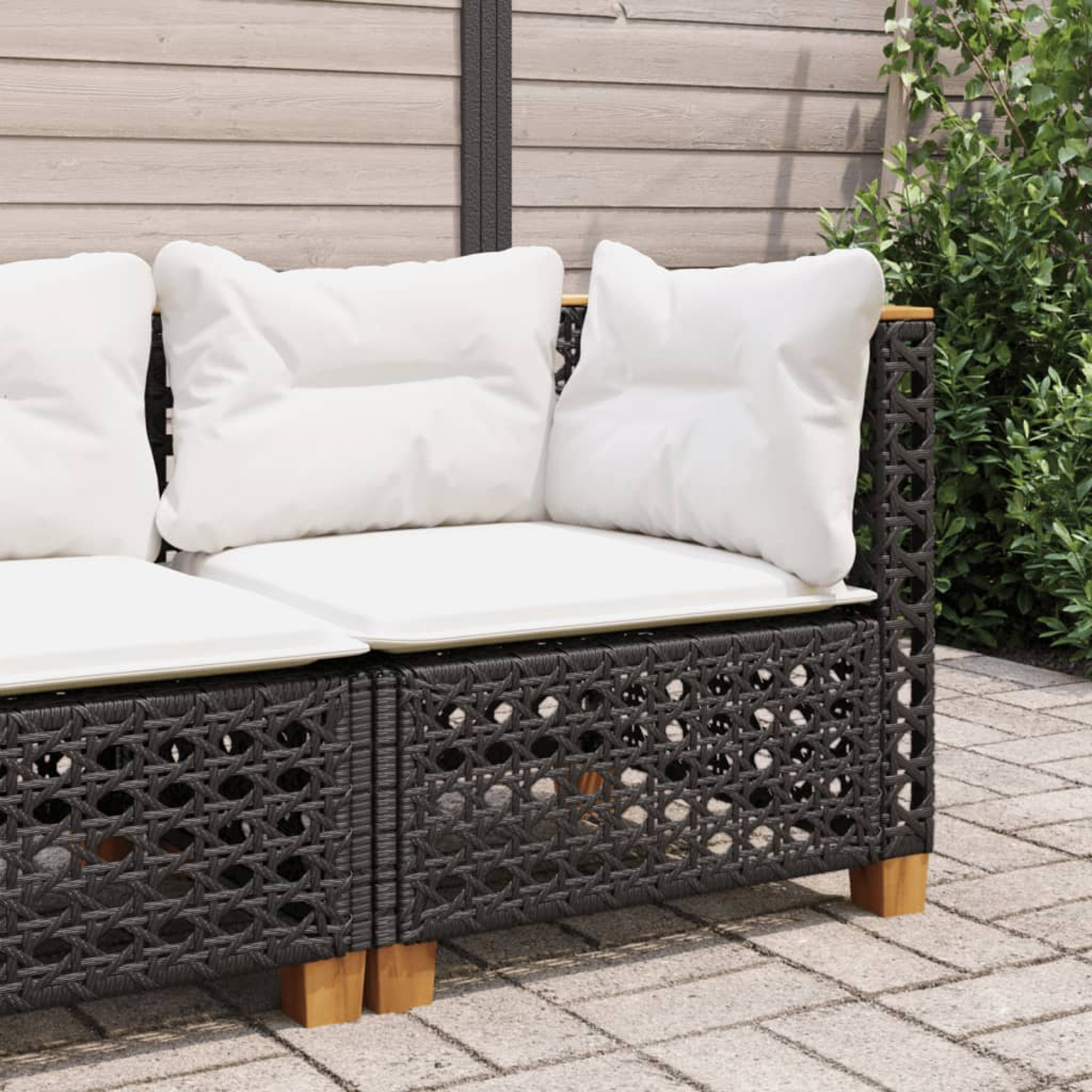 Nahaufnahme eines schwarzen Rattan-Sofas. Weiße Kissen auf den Sitzen. Terrasse.