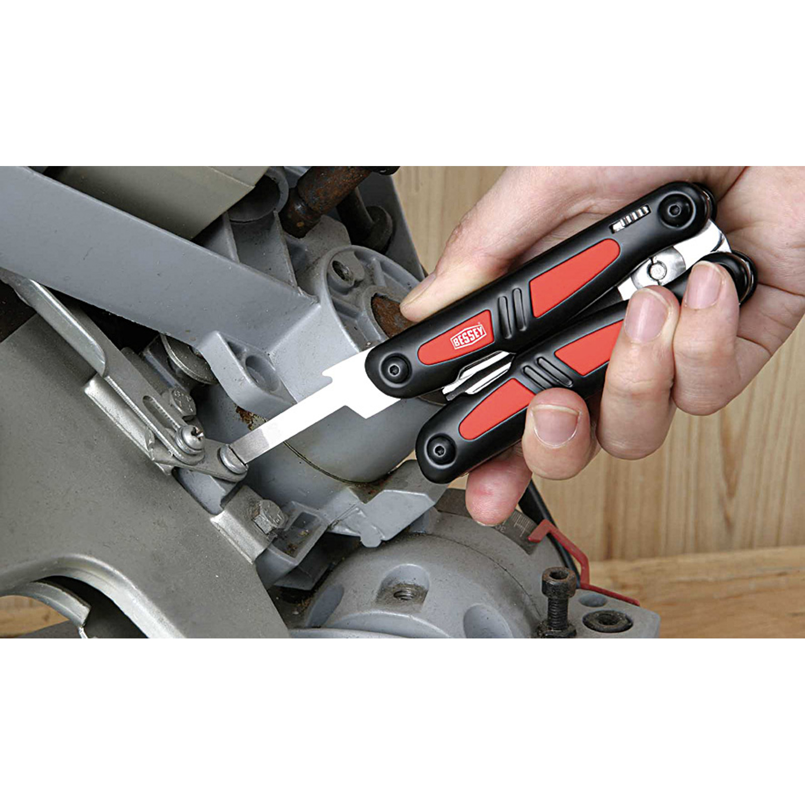 Mano che tiene un multi-tool vicino a un pezzo di macchina. Impugnatura rossa e nera.