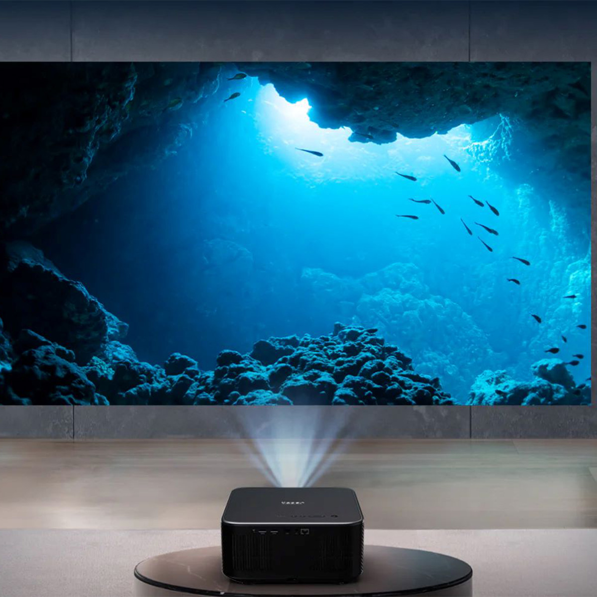 Czarny projektor wyświetlający podwodną scenę na dużym ekranie. Projektor znajduje się na dole.
