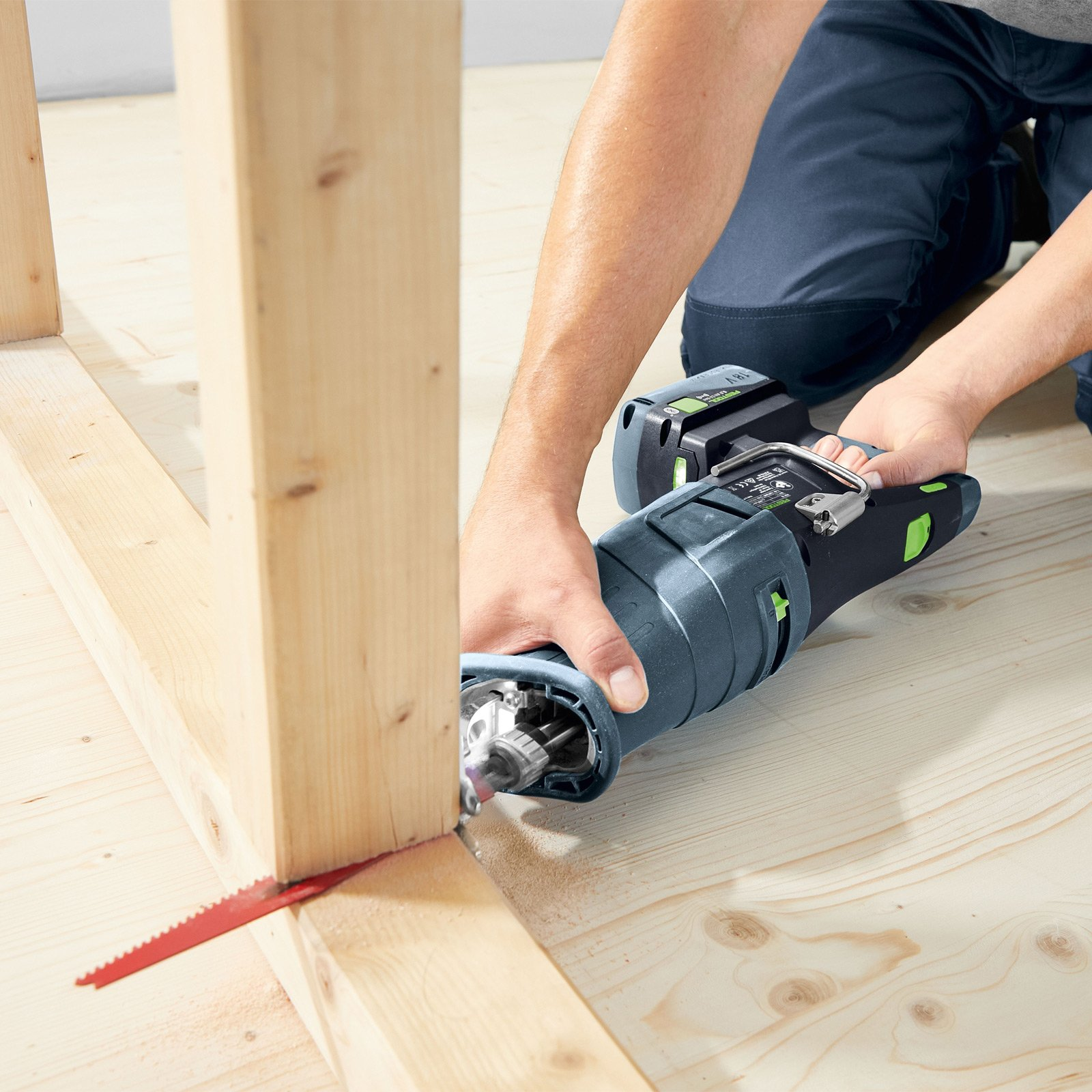 Una persona usa una sierra recíproca para cortar una viga de madera, en un suelo de madera.