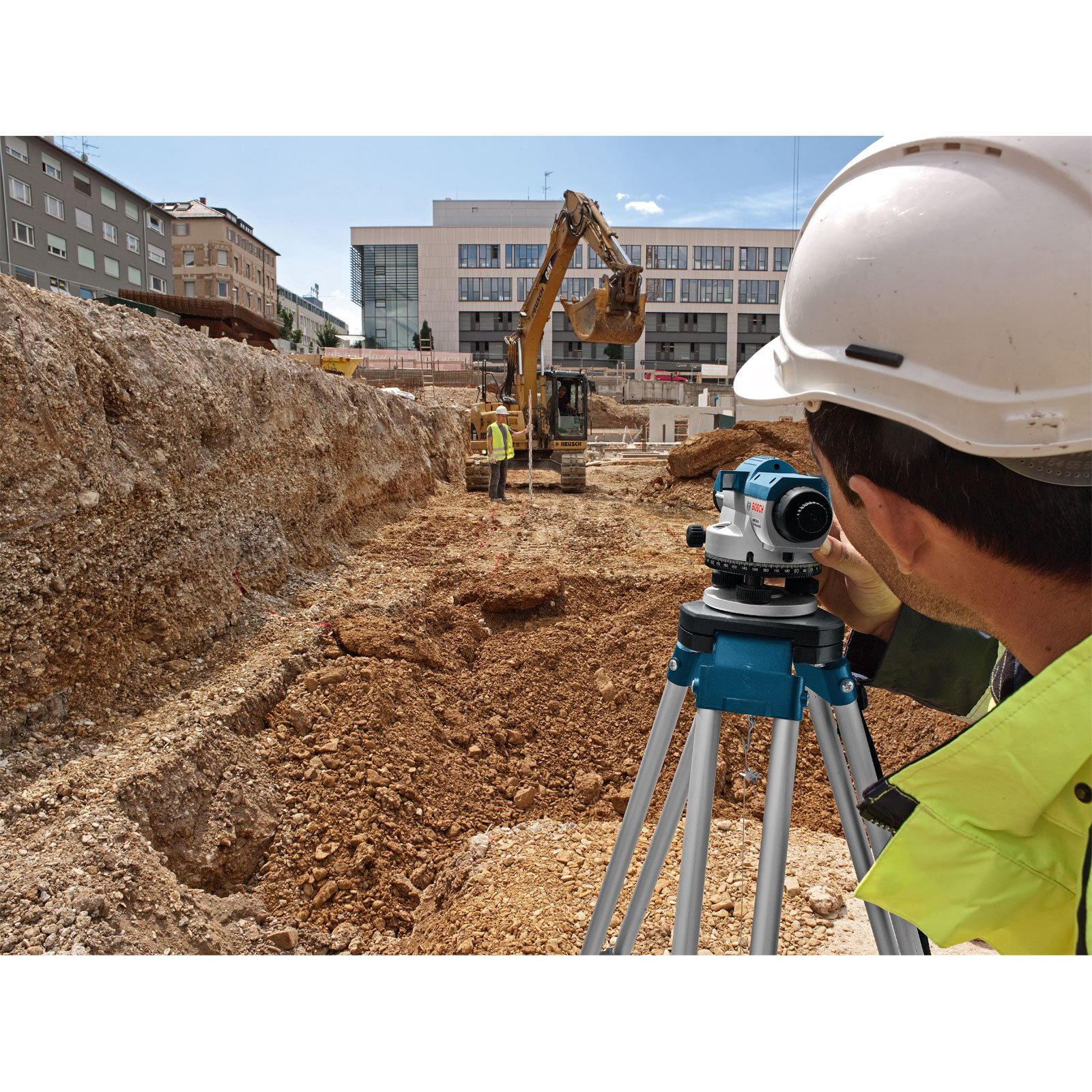 Mann benutzt eine Wasserwaage auf einer Baustelle. Ein Bagger im Hintergrund.