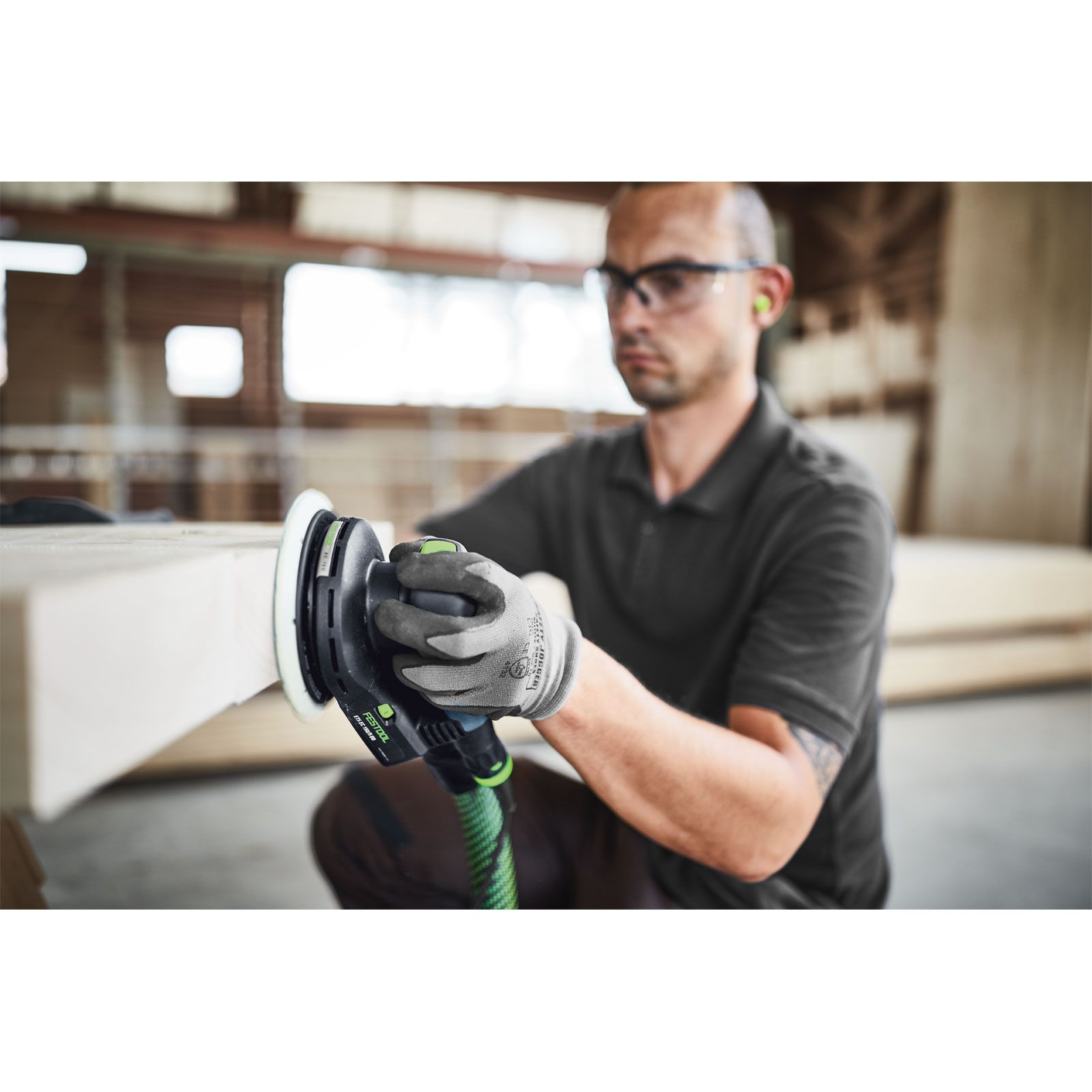 Un hombre usa una lijadora en una superficie de madera, con gafas de seguridad y tapones para los oídos.