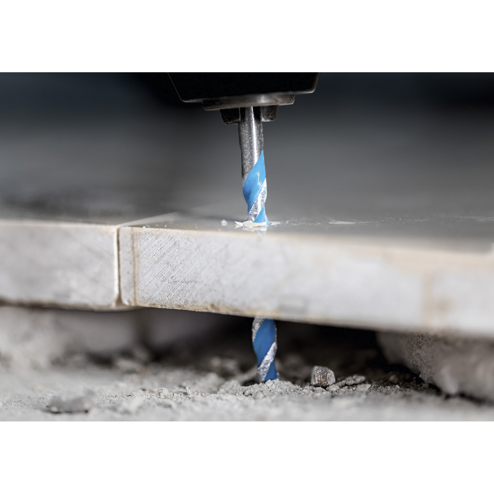 Zbliżenie wiertła wiercącego. Wiertło ma niebieskie spirale. Powierzchnia jest wiercona. Szare tło.