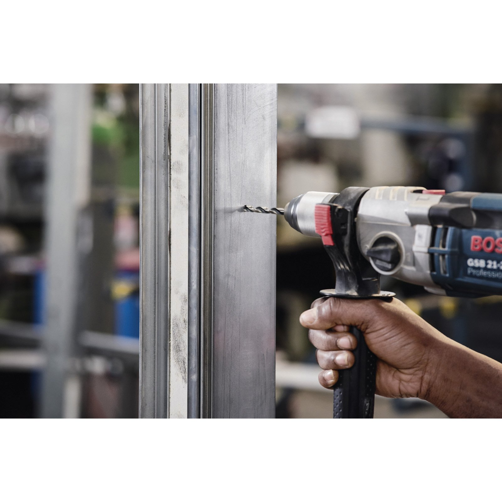 Wiertarka wierci otwór w metalowej belce. Ręka trzyma wiertarkę. Tło jest rozmyte.