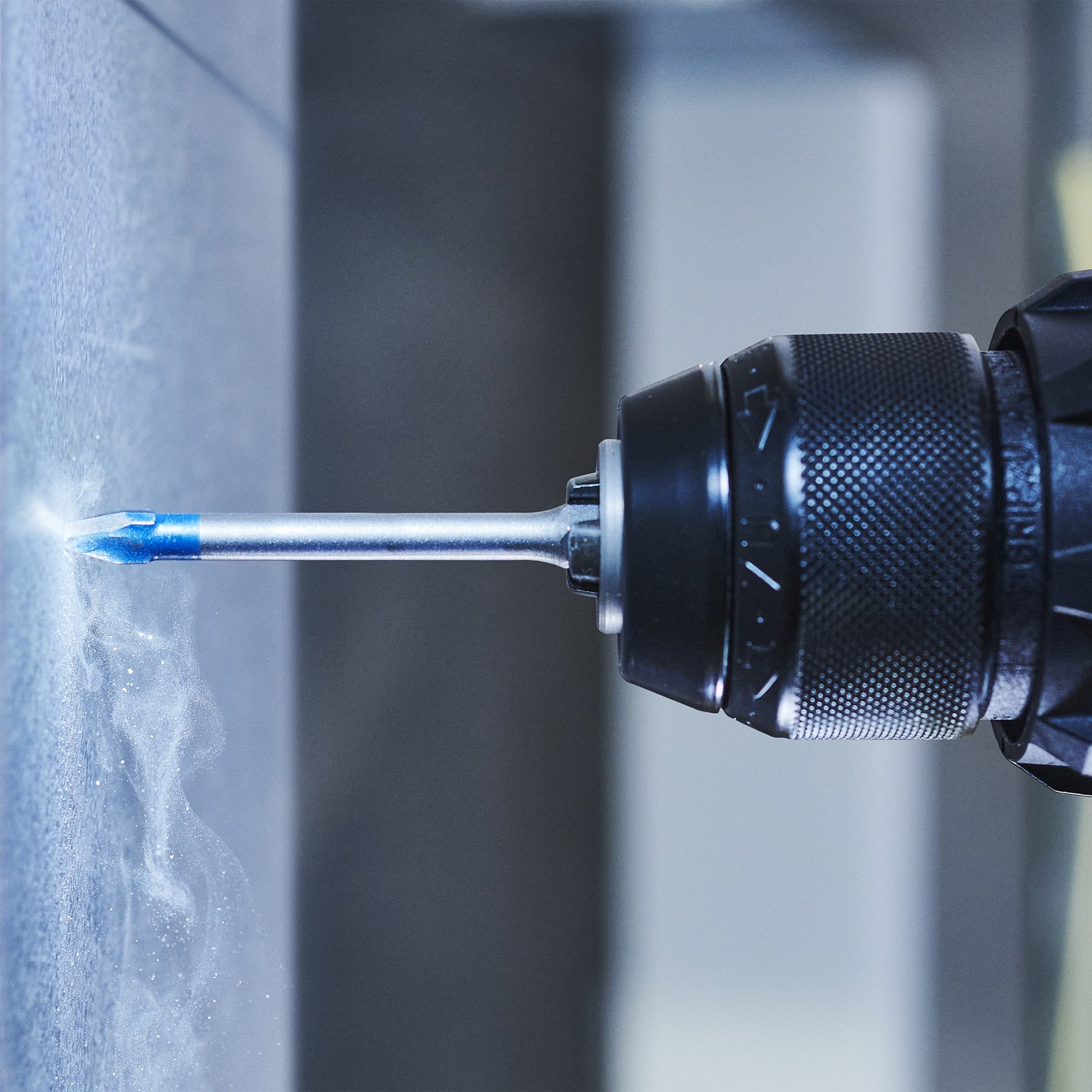 Wiertło wierci w powierzchni, generując pył. Wiertło i powierzchnia są ostre, na rozmytym tle.