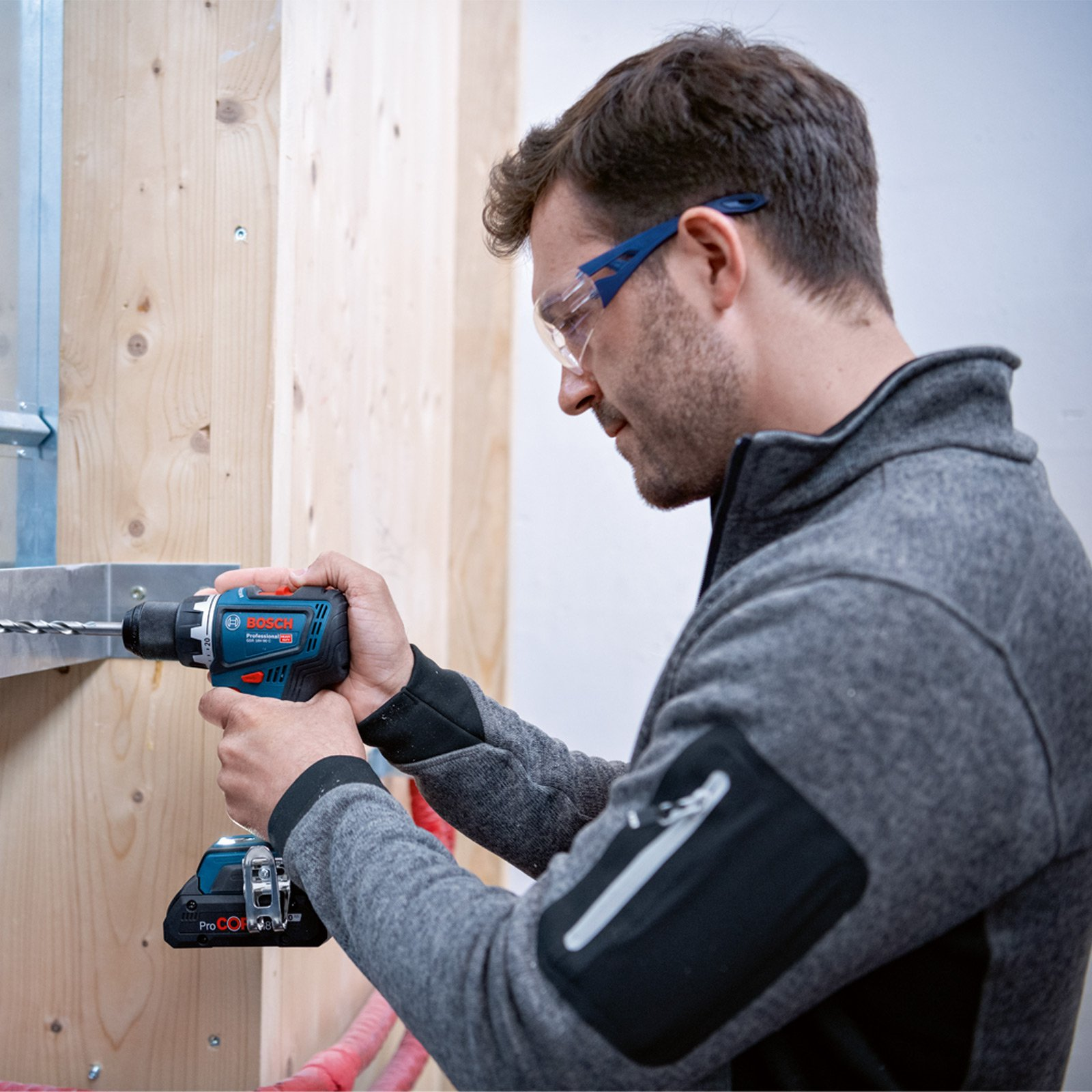 Un hombre taladra una estructura de madera con un taladro inalámbrico, usando gafas de seguridad.