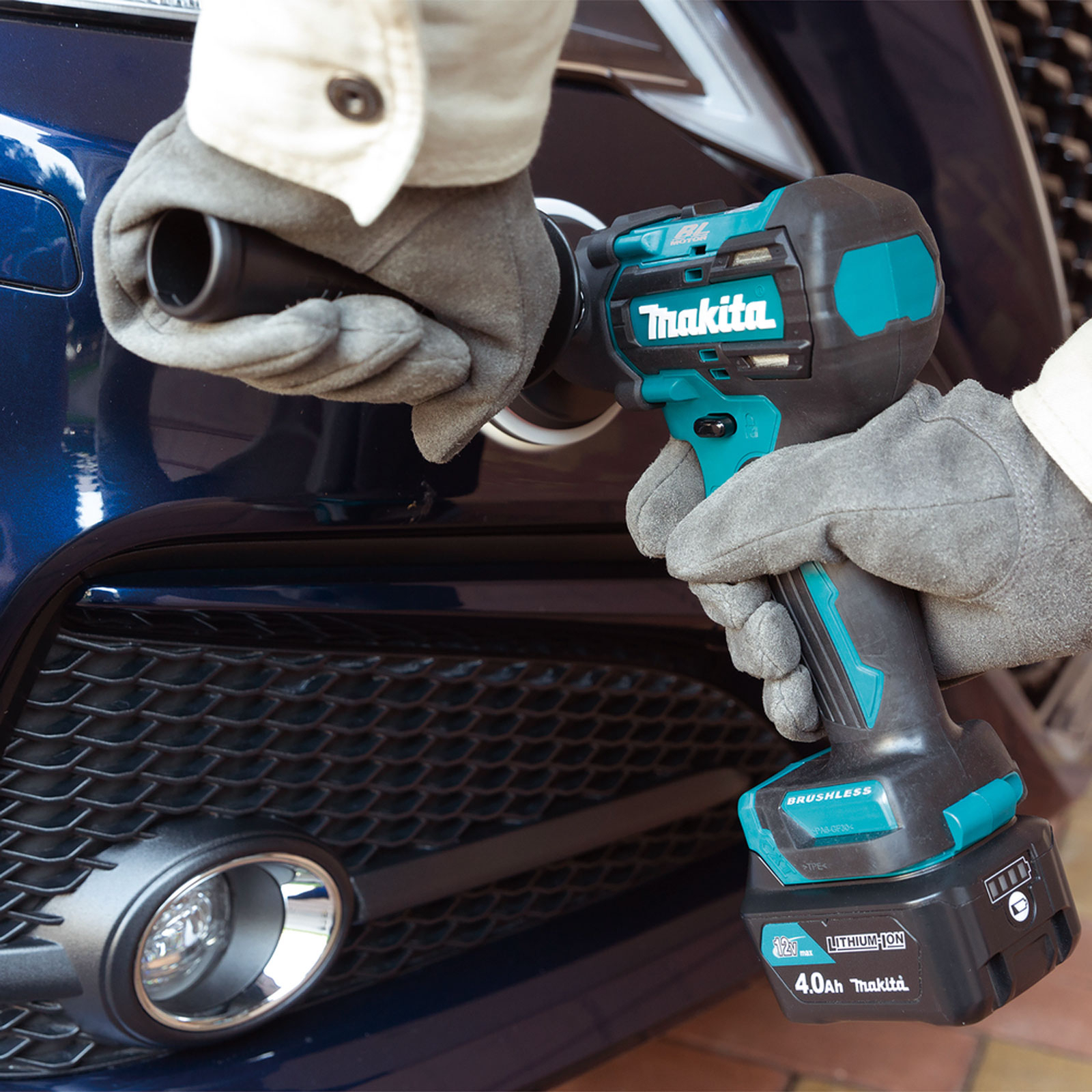 Una persona usa un elettroutensile Makita per lavorare su un'auto blu. Lo strumento è turchese e nero.