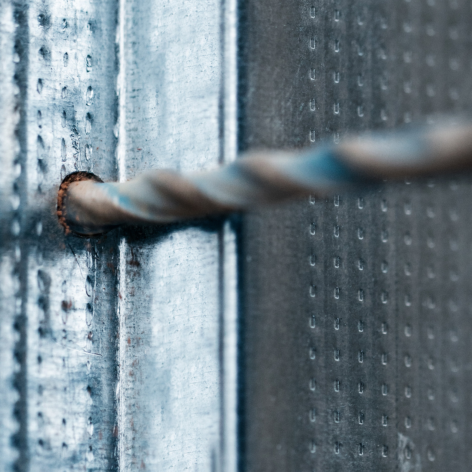 Zbliżenie metalowej powierzchni z otworem. Skręcony obiekt w kształcie liny przechodzi przez otwór. Widoczne krople wody.