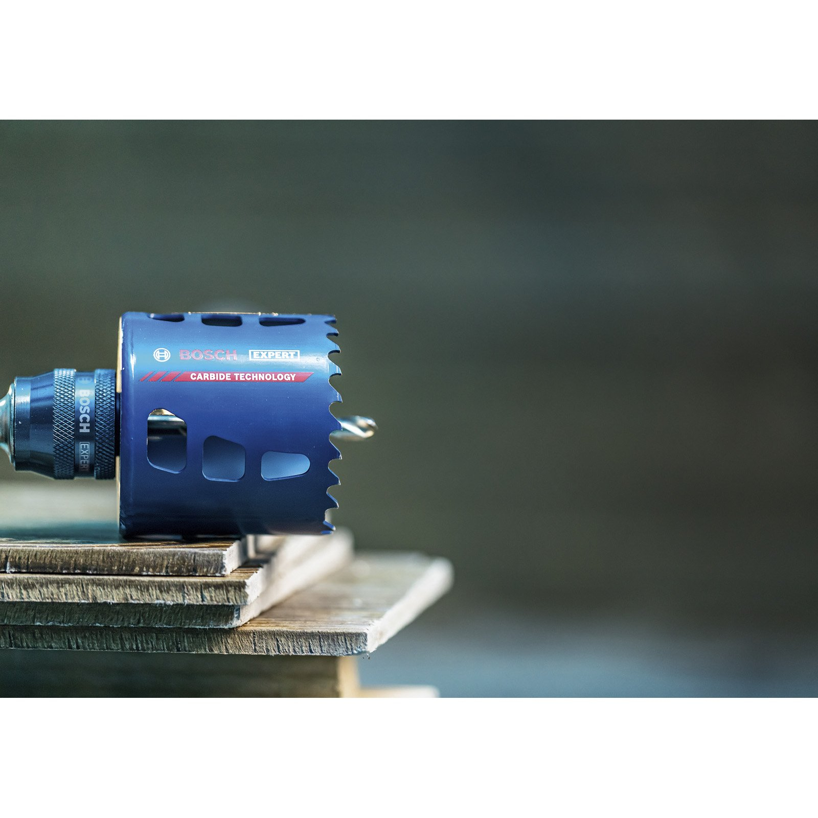 Niebieska piła otwornica Bosch Expert z węglików spiekanych na drewnianych deskach. Tło jest rozmyte zielone.
