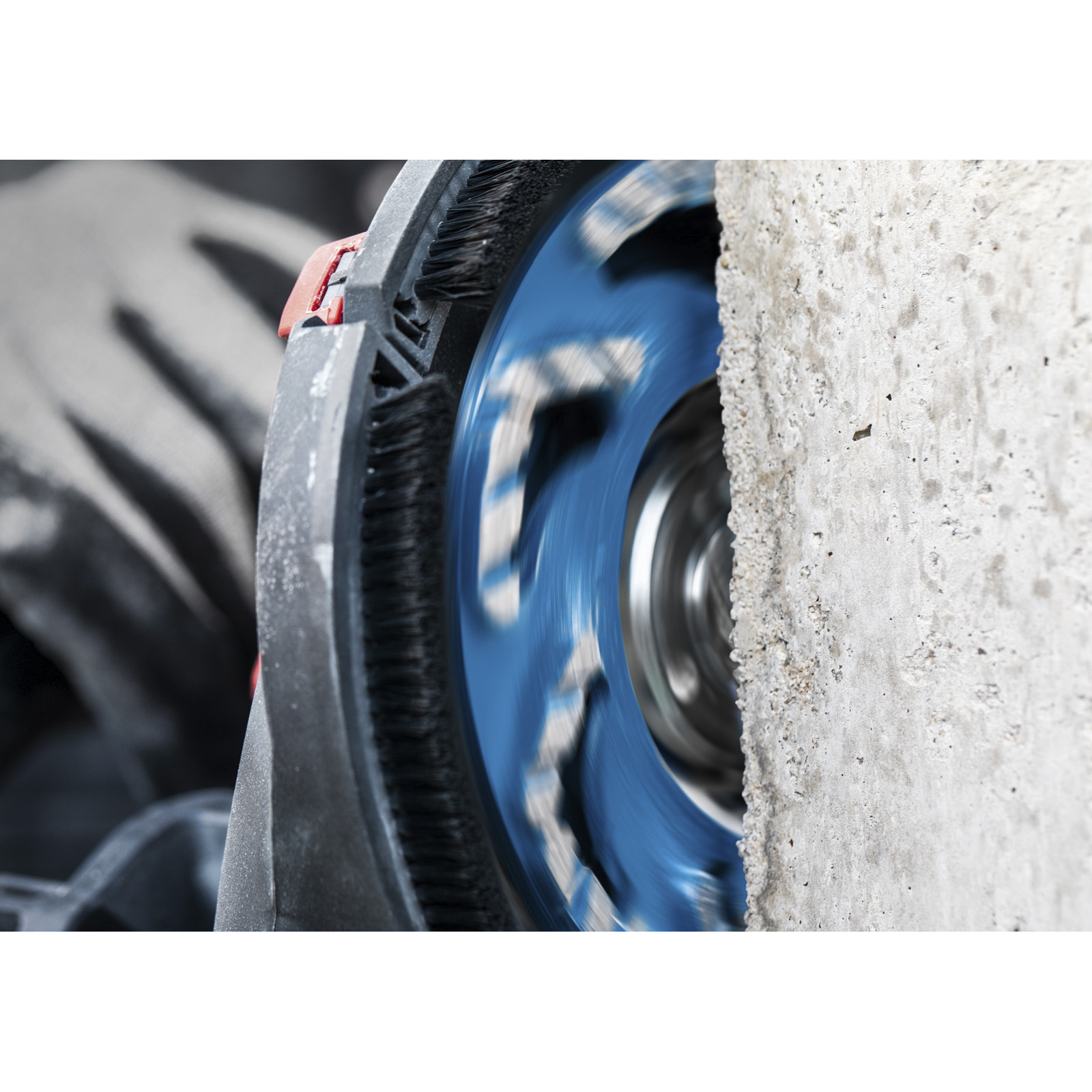 Eine blaue Schleifscheibe schleift Beton. Eine Hand hält das Werkzeug. Der Beton ist rau.