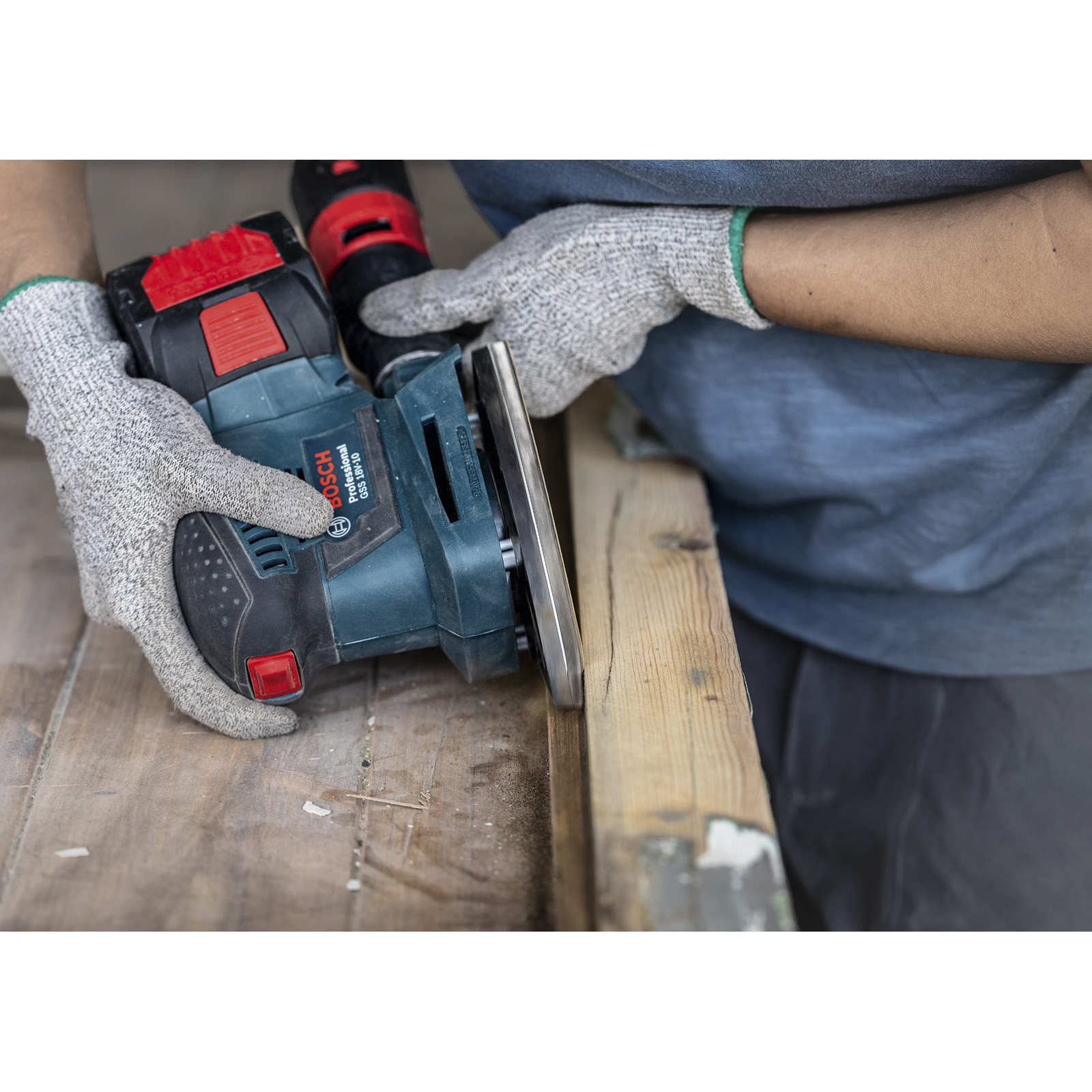 Eine Person benutzt einen Elektroschleifer auf Holz. Sie trägt Handschuhe. Der Schleifer ist blau und schwarz. Holz ist im Vordergrund.