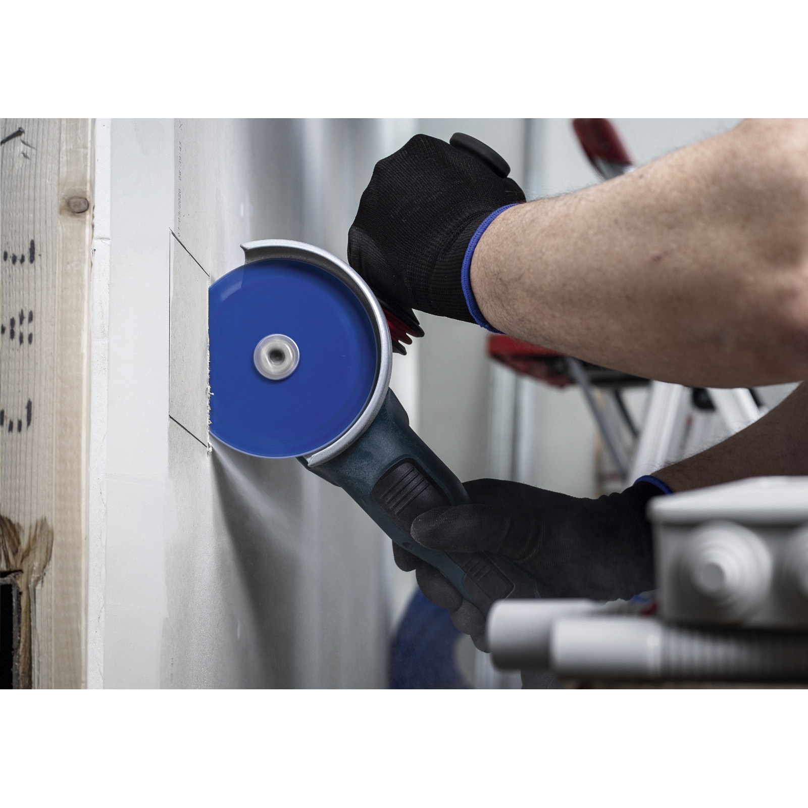 Eine Person schneidet mit einem Winkelschleifer und blauer Scheibe in eine weiße Wand. Die Person trägt Handschuhe.