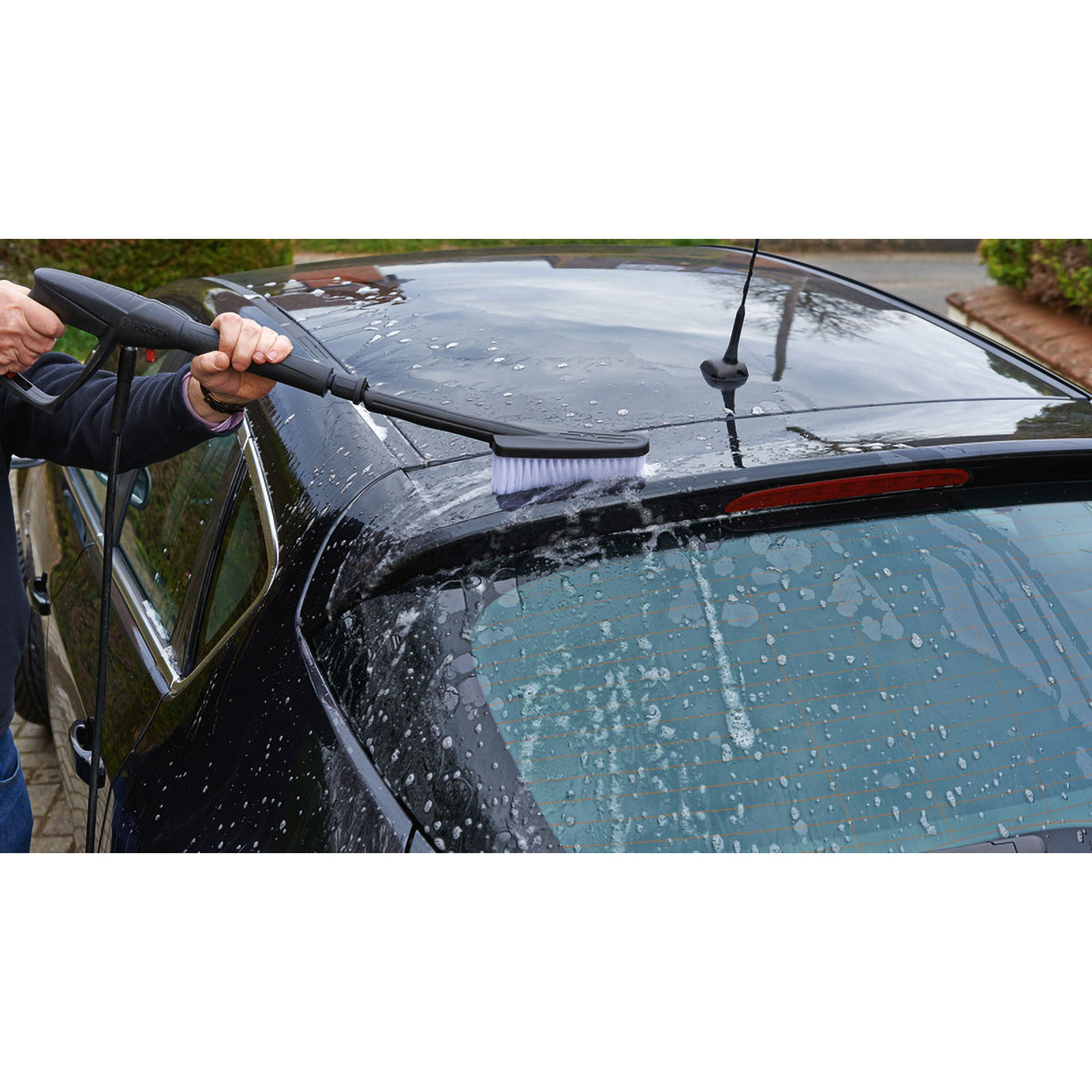 Eine Person wäscht ein schwarzes Auto mit einer Bürste. Seife und Wasser sind auf dem Auto. Das Auto hat ein Fenster und eine Antenne.