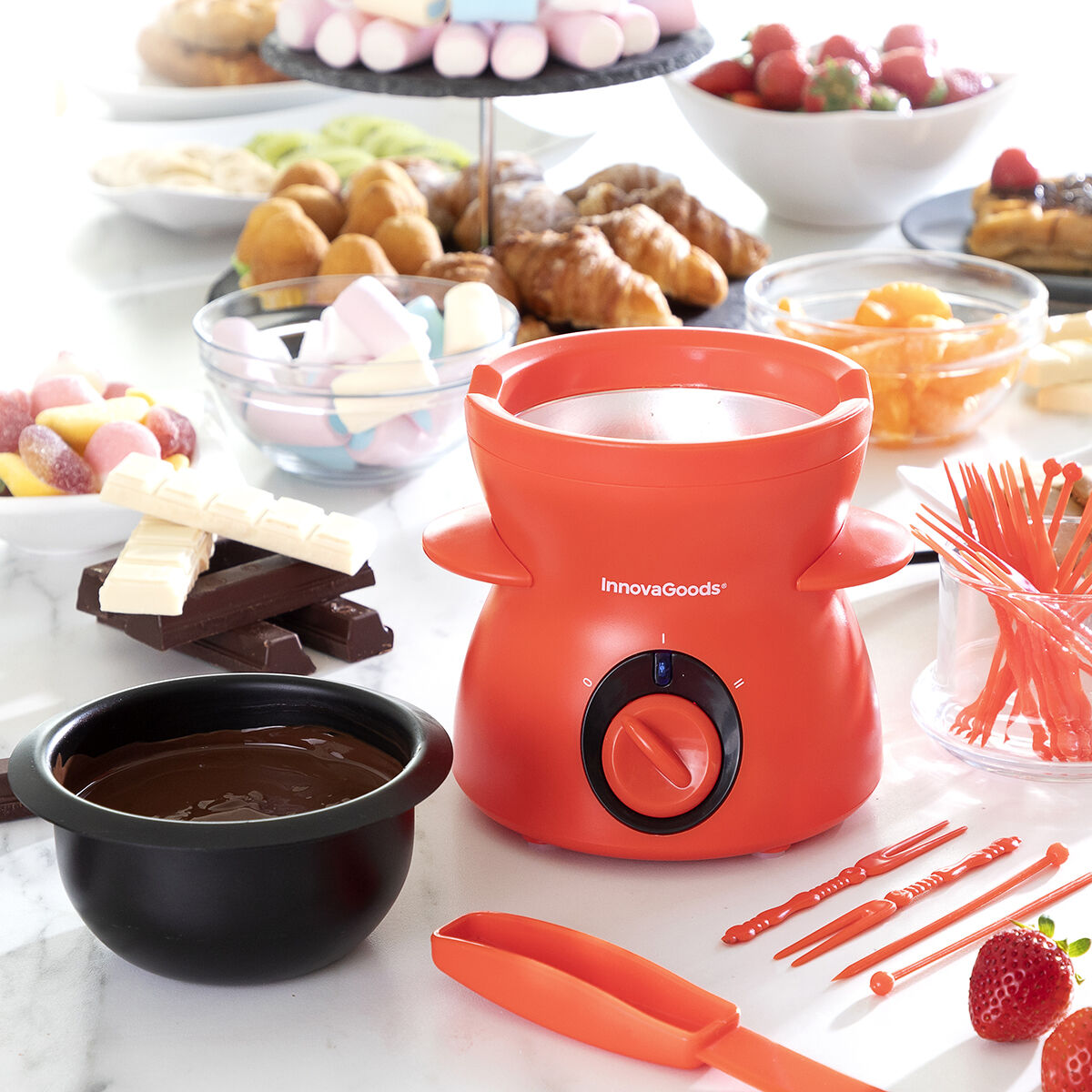 Oranges InnovaGoods-Fondue-Set mit Schokolade, Obst und Süßigkeiten. Enthält Schalen mit Erdbeeren, Marshmallows und Schokoriegeln.
