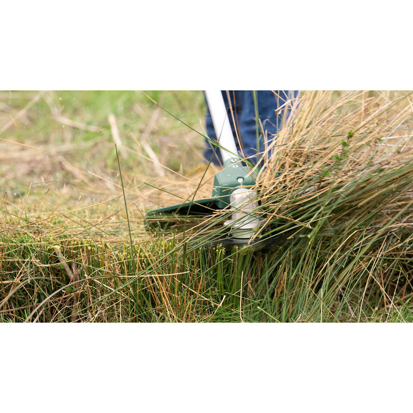 Eine Person schneidet mit einem Rasentrimmer hohes Gras. Das Gerät ist grün, das Gras ist braun und grün.