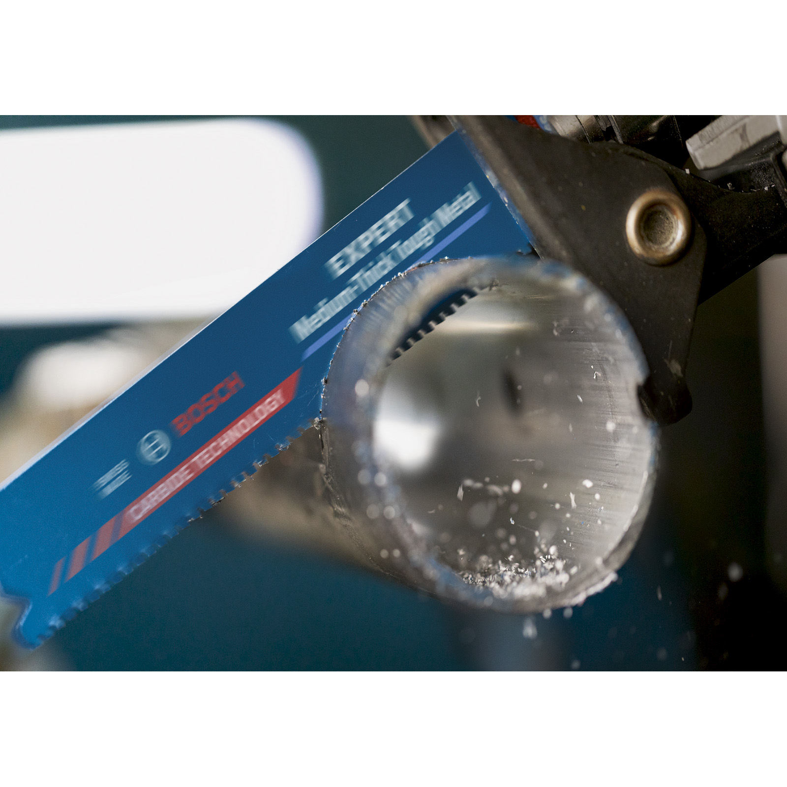 Niebieskie ostrze piły Bosch tnie srebrną metalową rurę. Piła trzymana jest przez czarne narzędzie. Widoczne są białe wióry.