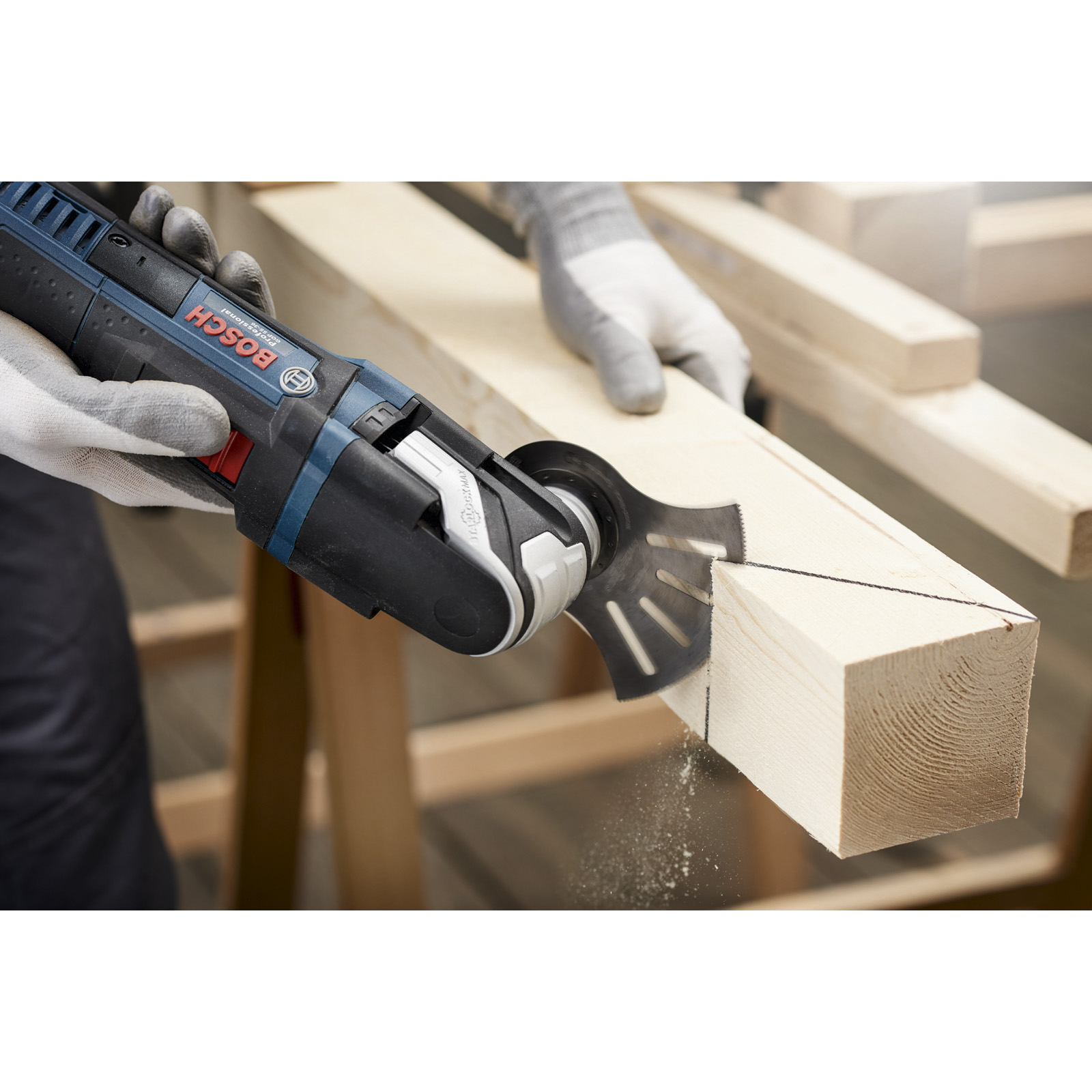 Eine Person schneidet mit einem Bosch-Multitool ein Holzbrett. Sägeblatt schneidet durch das Holz. Hände mit Handschuhen.