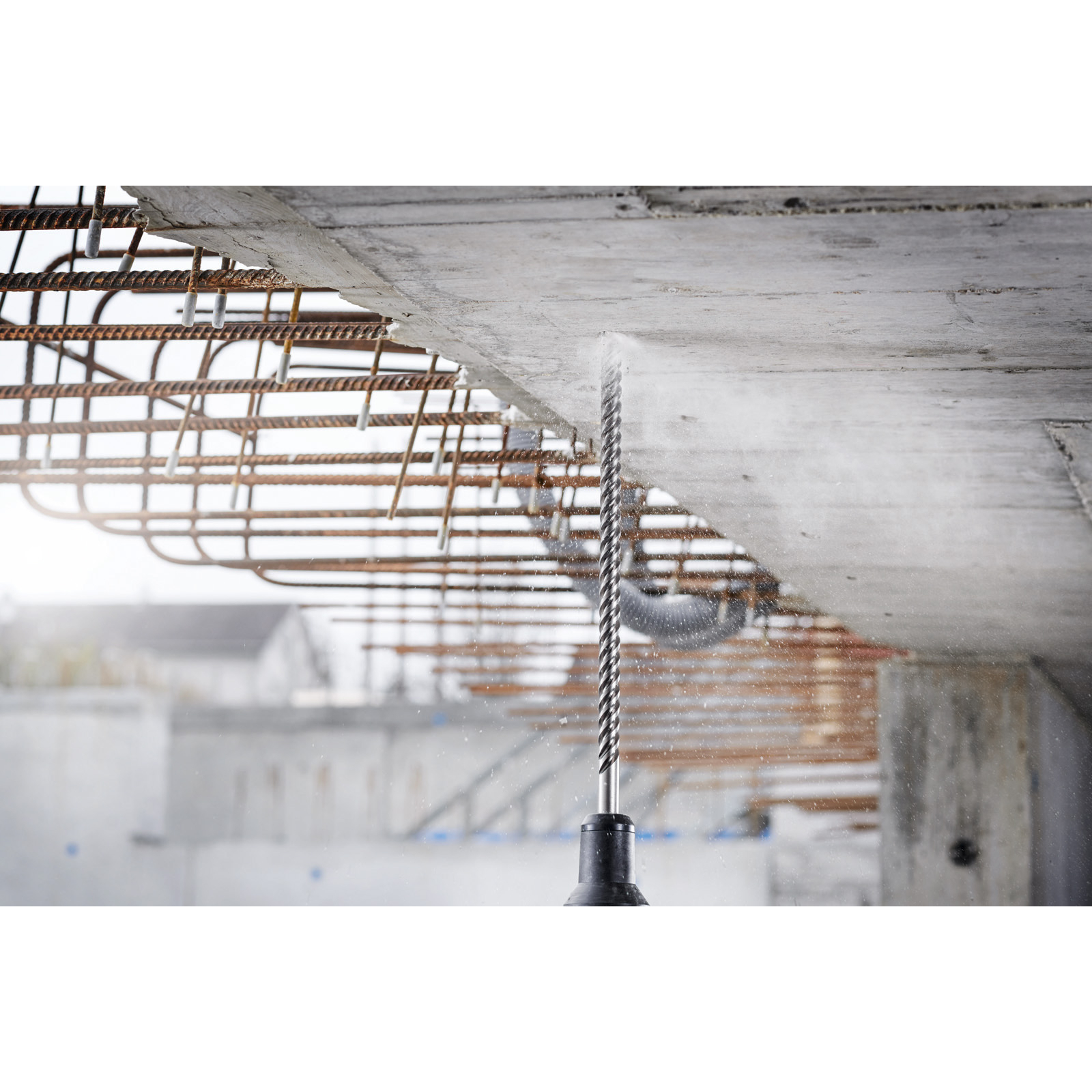Ein Bohrer bohrt in Beton mit Bewehrung und erzeugt Staub. Bauen im Bauwesen.