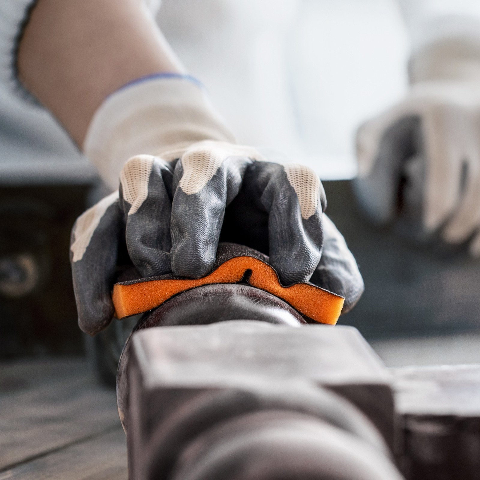 Behandschuhte Hand hält einen orangefarbenen Schleifschwamm über einem dunklen, abgerundeten Objekt, möglicherweise für die Holzbearbeitung.