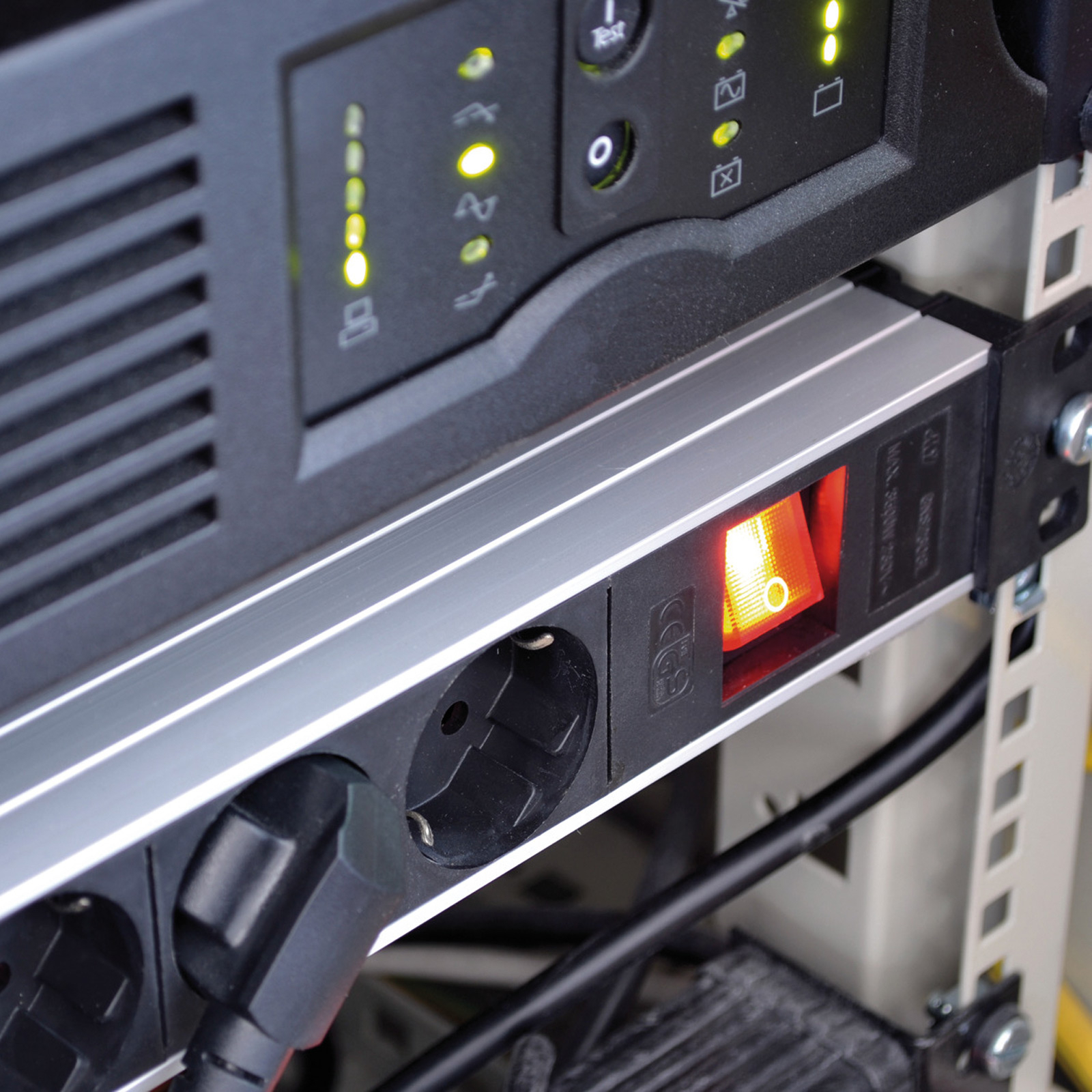 Zbliżenie listwy zasilającej do szafy serwerowej z podświetlanym przełącznikiem, gniazdami i podłączonym przewodem zasilającym. Widoczne są również diody LED.