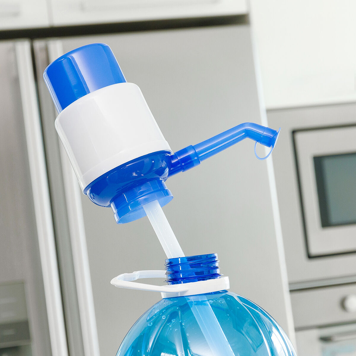 Eine blau-weiße Wasserpumpe befindet sich auf einer blauen Wasserflasche. Im Hintergrund ist eine Küche mit Kühlschrank und Ofen zu sehen.