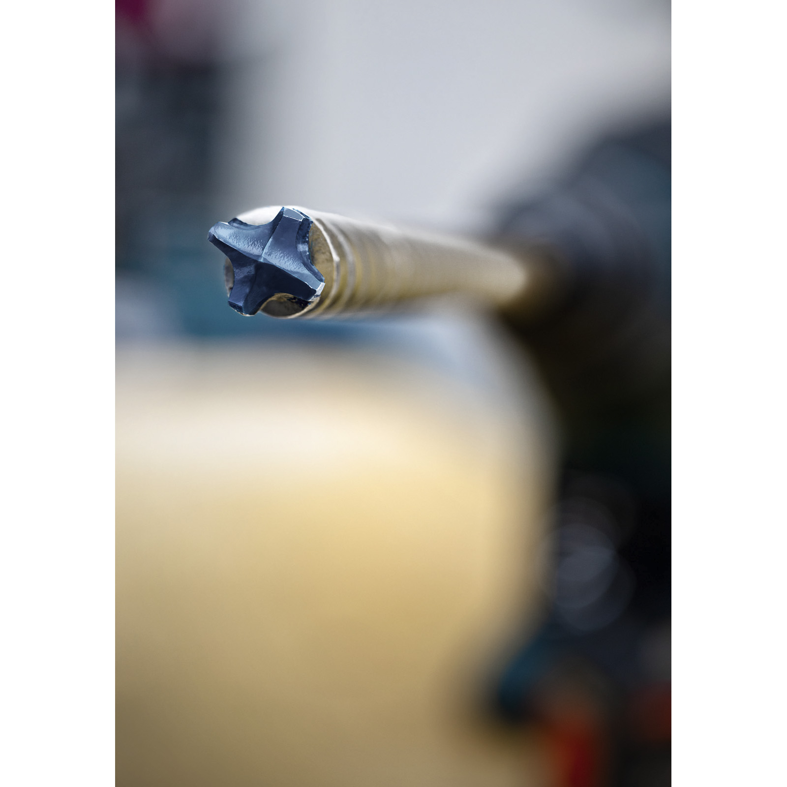 Zbliżenie wiertła, głowica w kształcie gwiazdy. Wiertło jest metalowe. Tło jest rozmyte.