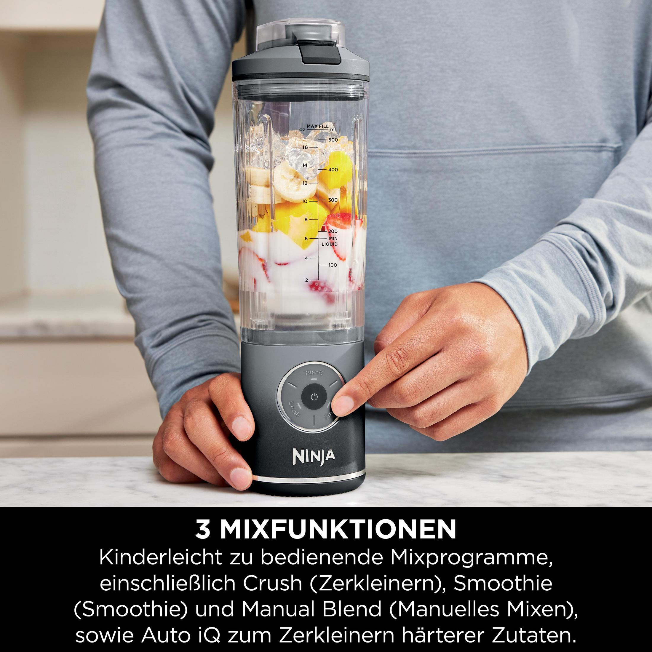 Person benutzt Mixer mit Zutaten. Graues Gerät mit Knopf, Hand auf dem Gerät.