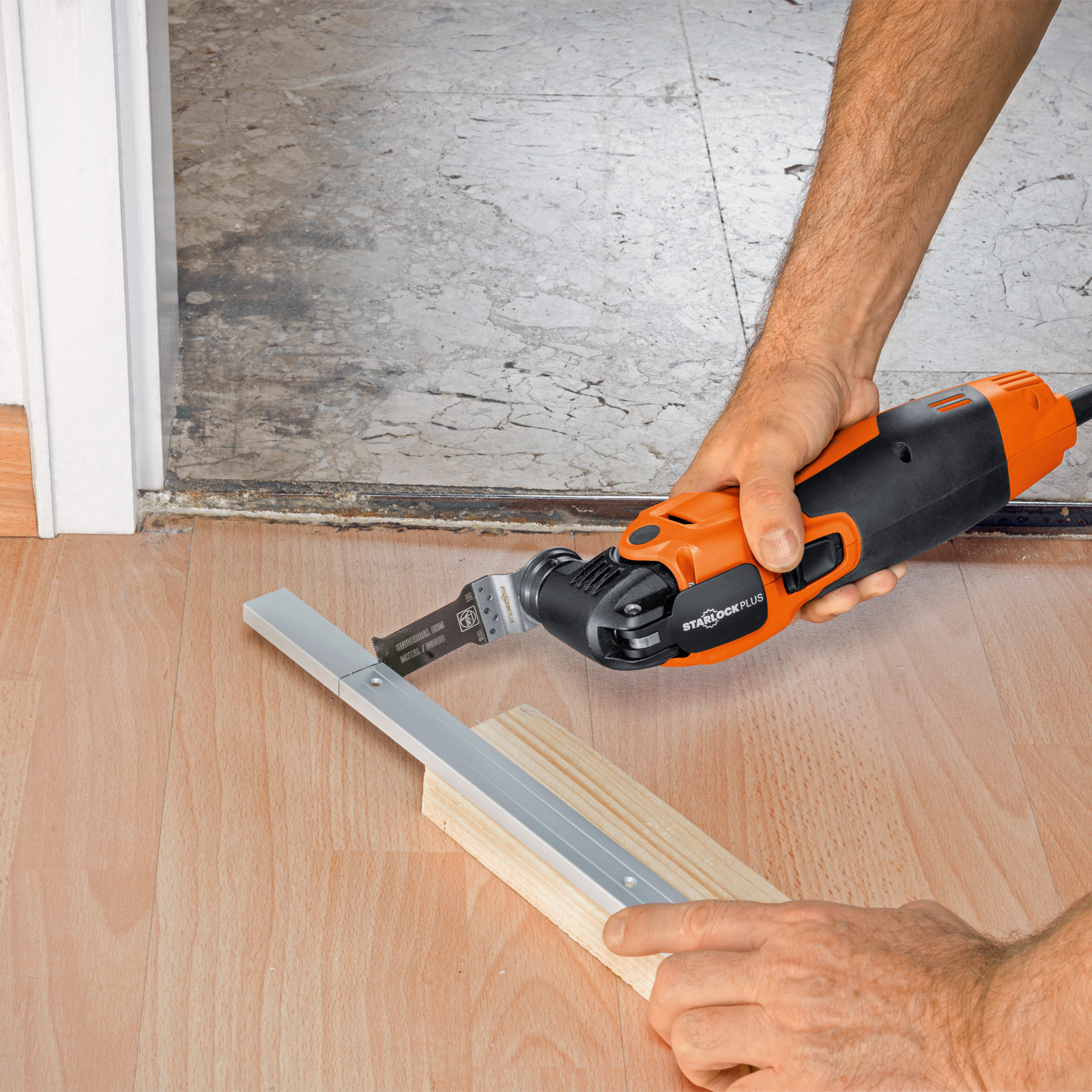 Eine Person schneidet mit einer Säge einen Metallstreifen auf Holzblöcken auf einem Holzboden. Die Säge ist orange und schwarz.