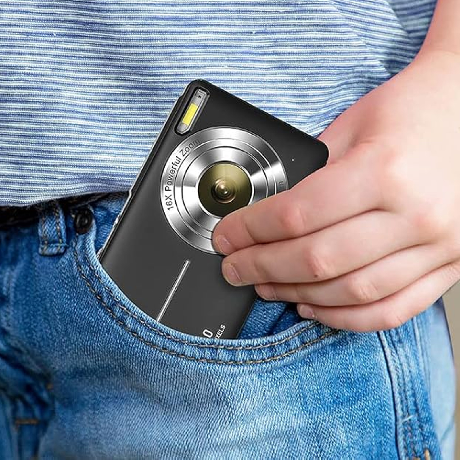 Eine schwarze Kamera mit silbernem Objektiv in einer Tasche. Eine Hand hält die Kamera, eine Person trägt Jeans.