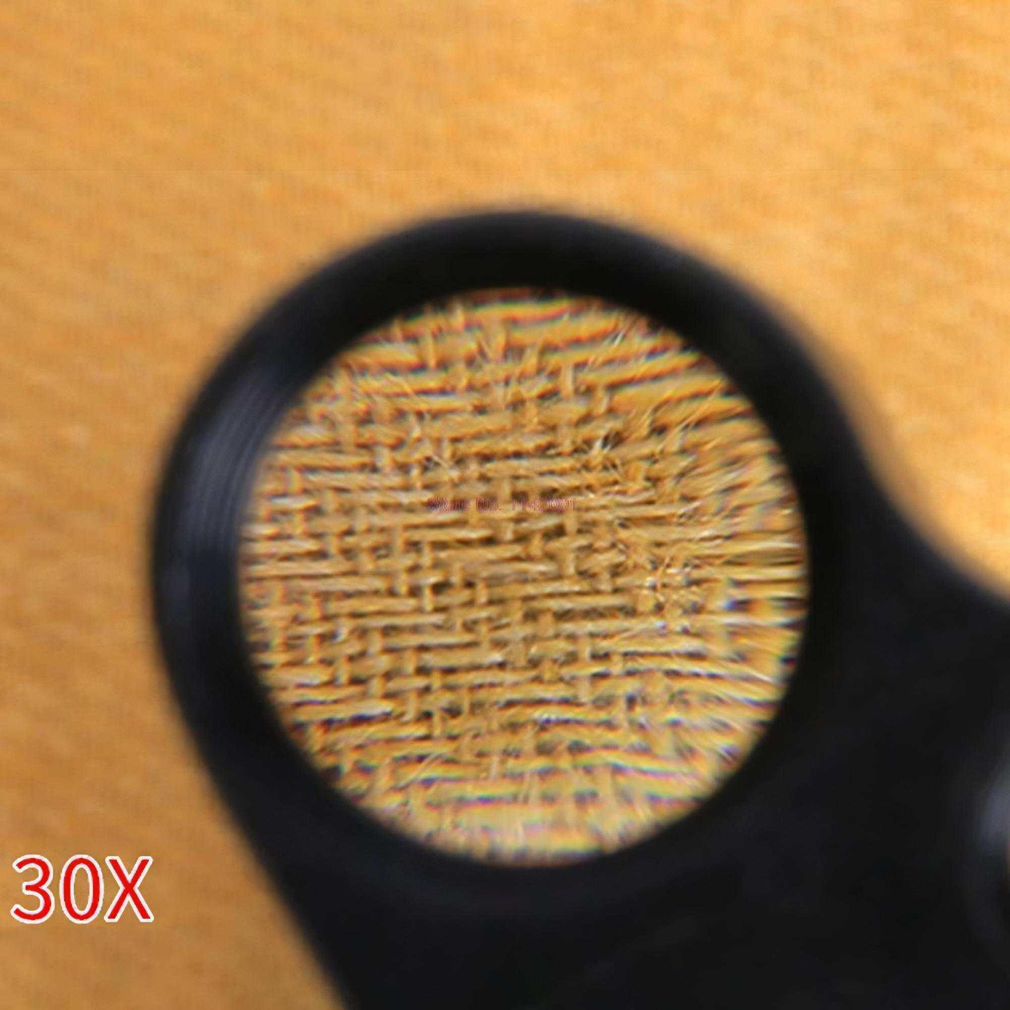 Eine Lupe zeigt gewebtes Material. Das Glas hat einen schwarzen Rahmen und die Zahl 30X befindet sich unten links.