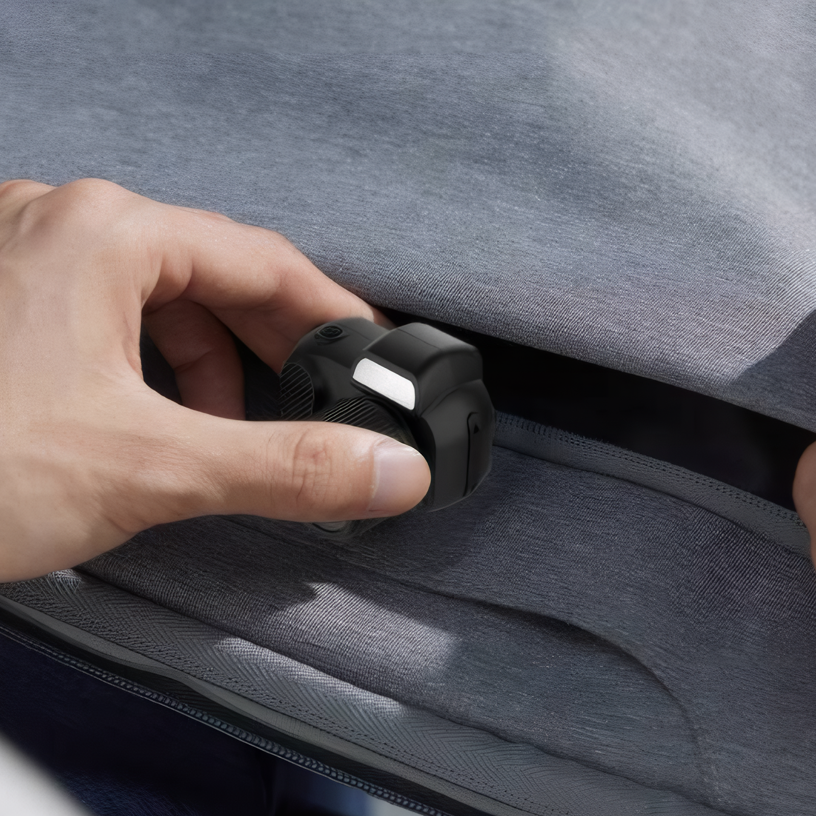 Hand steckt eine schwarze Kamera in eine graue Tasche. Die Kamera hat ein weißes Licht. Die Tasche ist mit Reißverschluss.