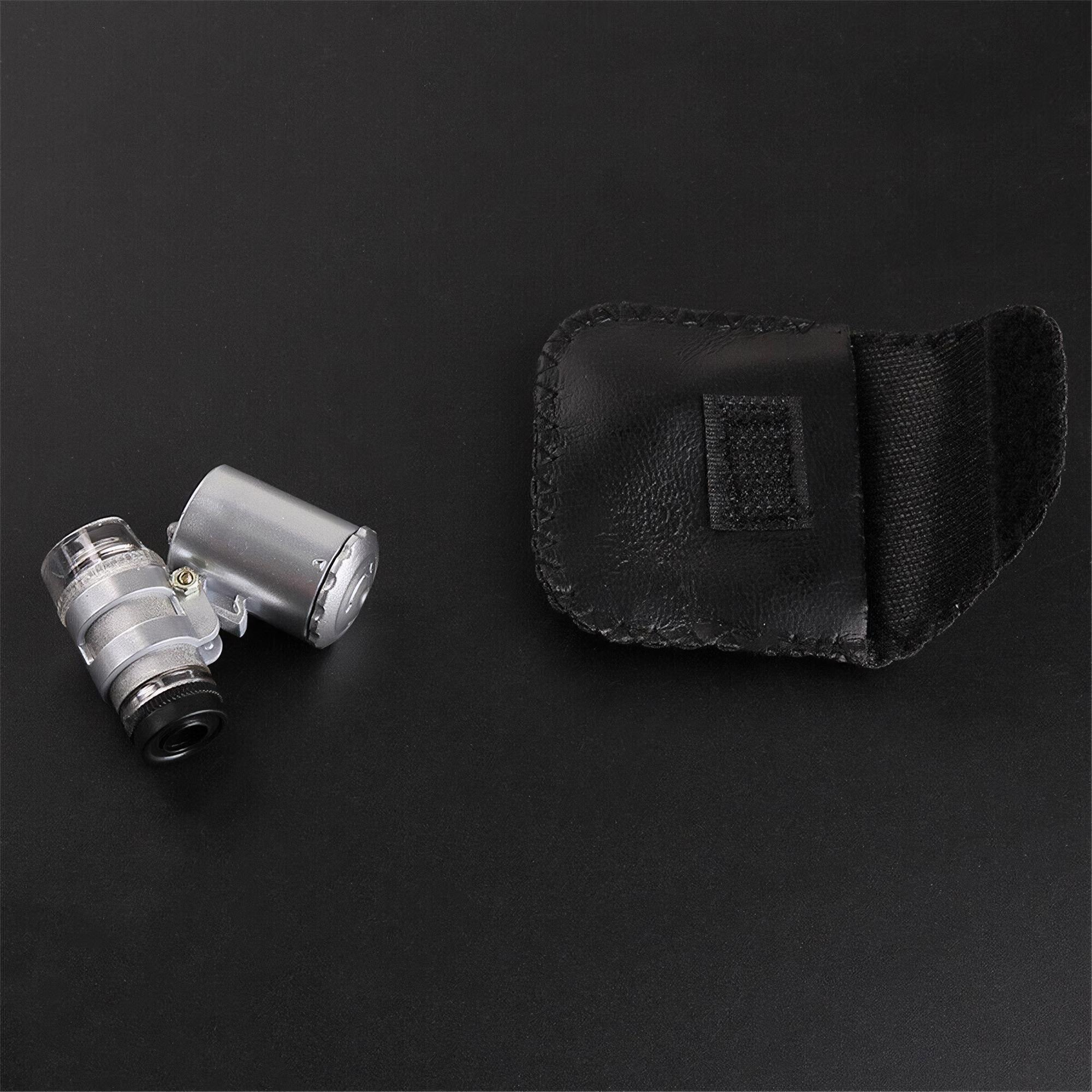 Eine silberne Lupe und ein schwarzes Etui liegen auf einer schwarzen Oberfläche. Die Lupe ist detailliert; das Etui ist geöffnet.