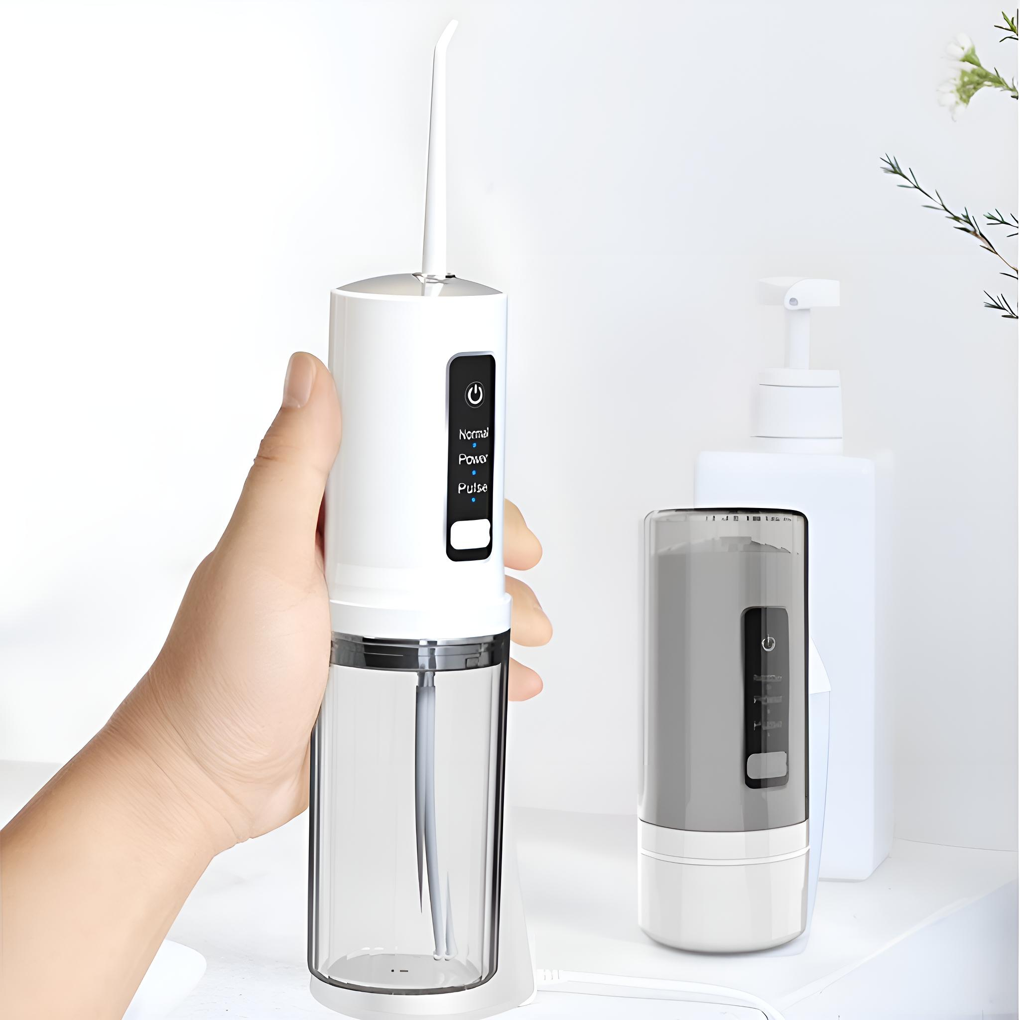 Eine Hand hält einen weißen und klaren Wasserflosser. Ein zweiter Flosser und eine Flasche befinden sich im Hintergrund auf einer weißen Oberfläche.