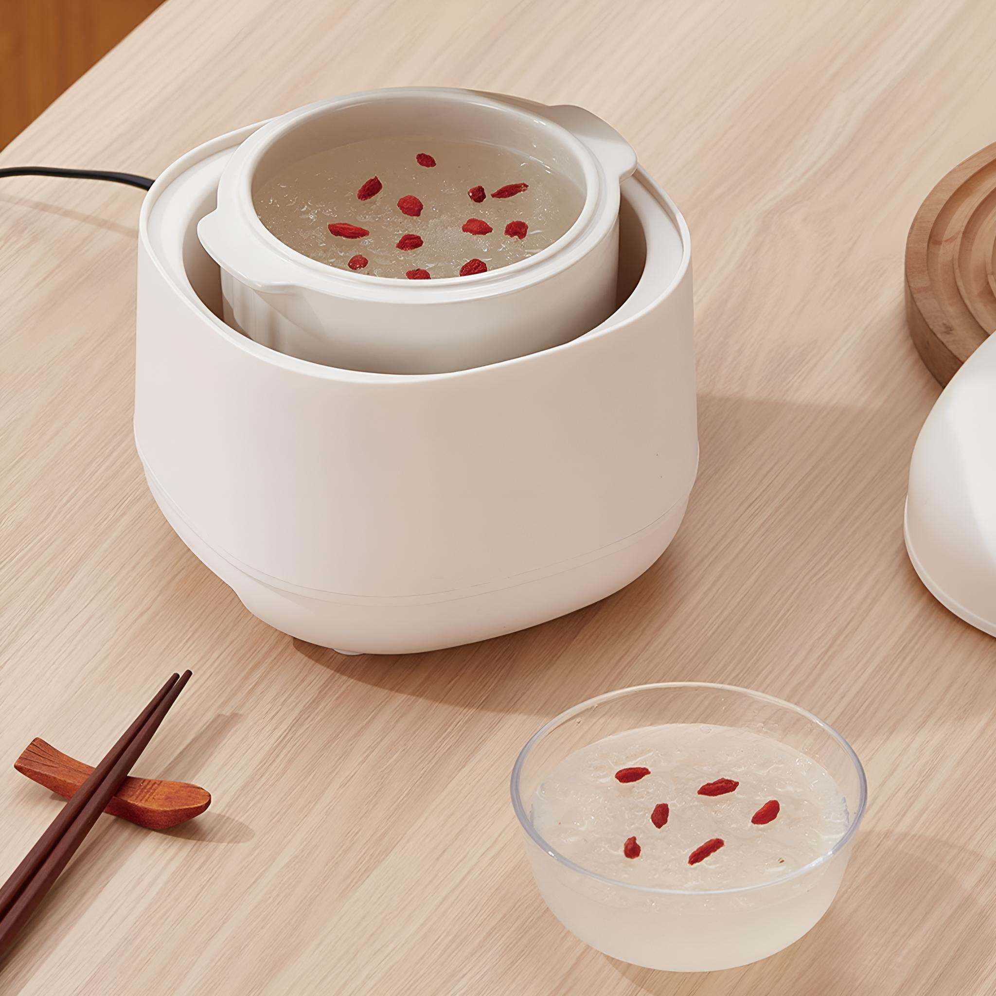 Weißes Gerät mit Schüssel mit Essen und roten Beeren. Schüssel mit Essen mit roten Beeren auf einem Holztisch.